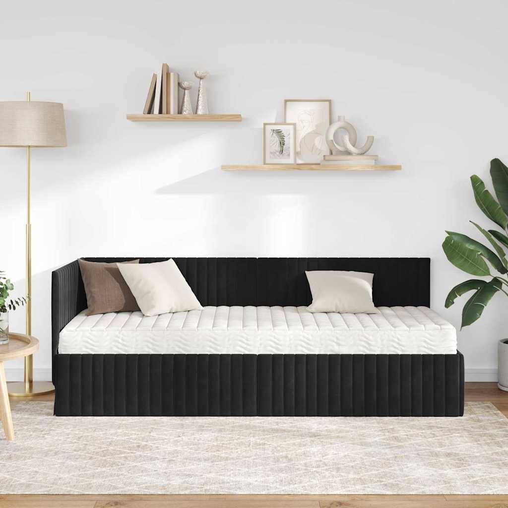 Ein moderner Wohnraum mit einem schwarzen Tagesbett, weißen Kissen, einem beigen Teppich, einer Zimmerpflanze, einer Stehlampe und zwei minimalistischen Wandregalen.