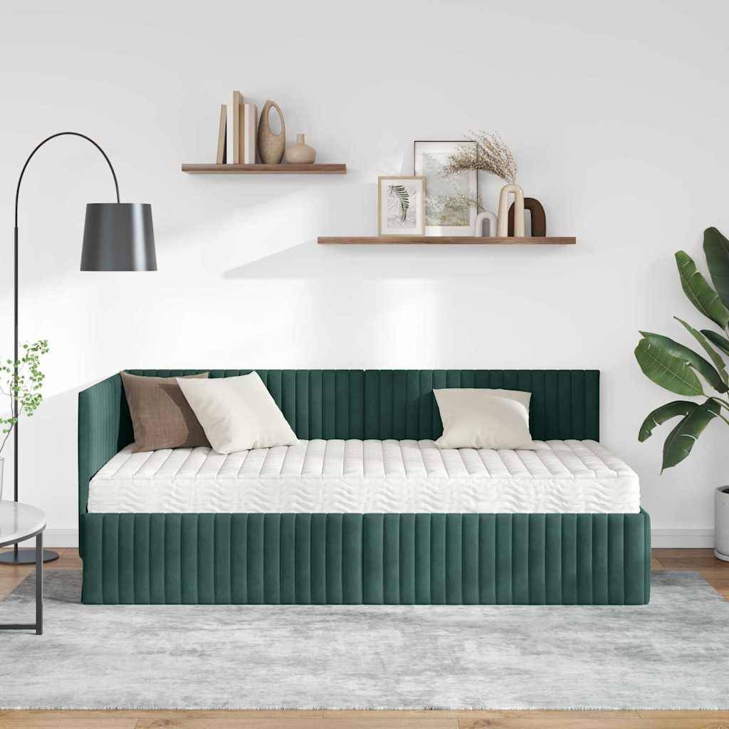 Ein minimalistisches Wohnzimmer mit einer grünen Samt-Liege, beige- und weißen Kissen, Holzregalen mit Dekoration, einer Stehlampe und Pflanzen.