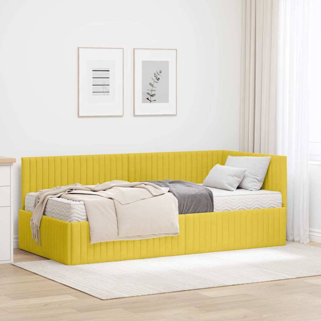 Ein gelbes Tagesbett mit grau-beiger Bettwäsche steht in einem minimalistischen Raum. Weiß gerahmte Kunst hängt darüber, und rechts befindet sich ein vorhanggefasster Fenster.