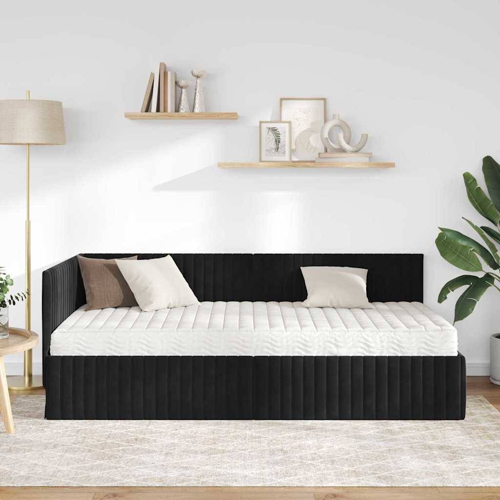 Ein Schlafzimmer zeigt ein schwarzes gepolstertes Tagesbett mit weißer Bettwäsche, begleitet von zwei Kissen. Eine Lampe, Regale und eine Pflanze ergänzen die Dekoration.