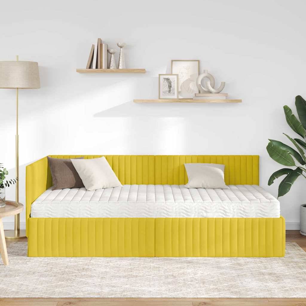 Ein gelbes Tagesbett mit neutralen Kissen in einem hellen Raum, mit einer Stehlampe, Wandregalen mit Dekorationen und einer großen Pflanze mit Blättern daneben.