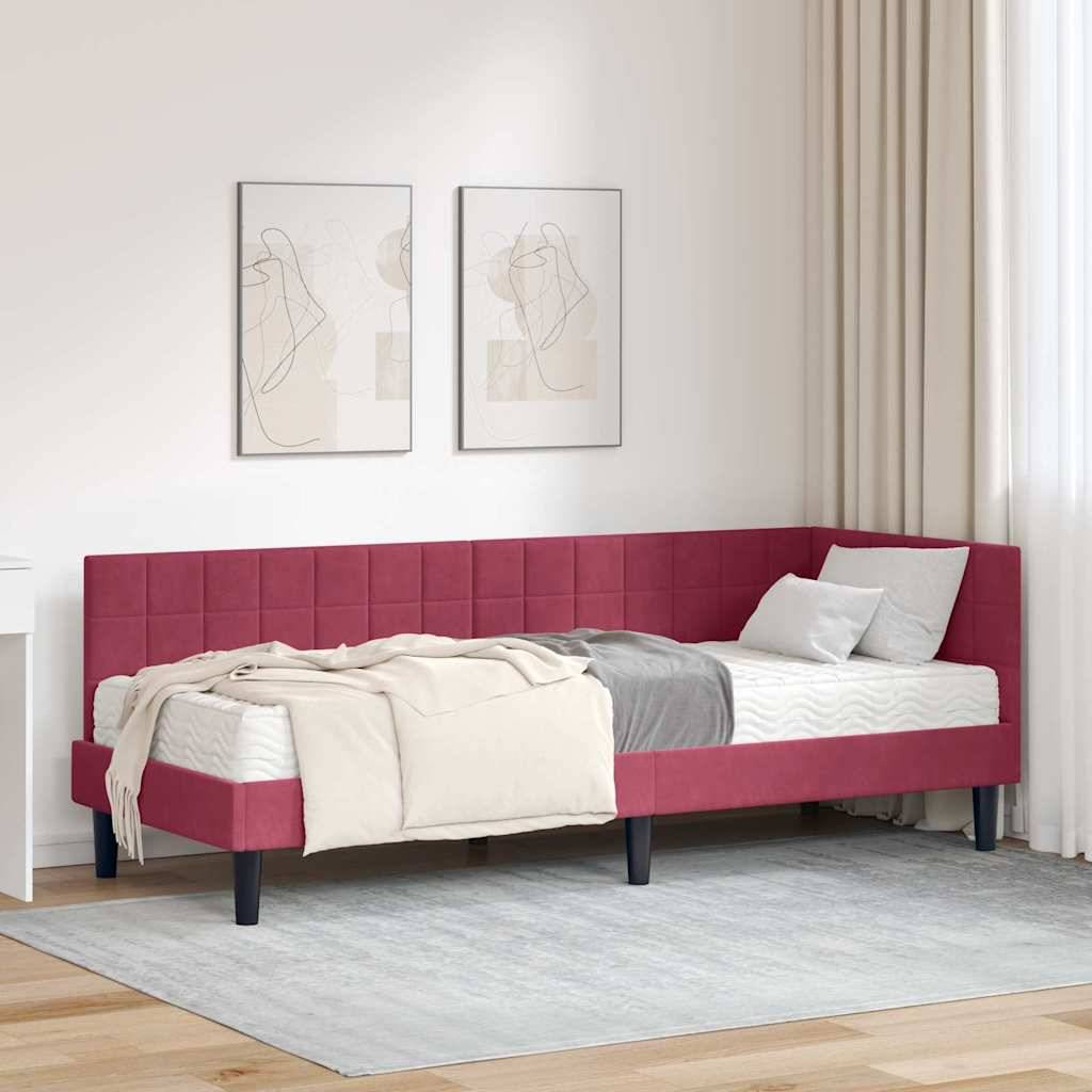 Ein roter gepolsterter Tagesbett mit Kissen und einer Decke steht vor einer weißen Wand mit abstrakten Kunstwerken. Ein kleiner Schreibtisch und ein Stuhl befinden sich in der Nähe.