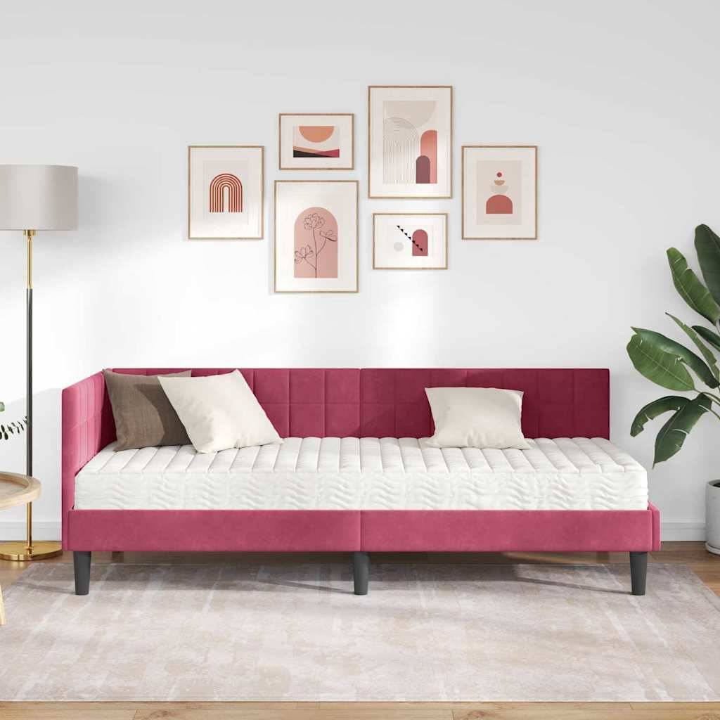 Ein modernes rosa Schlafsofa mit weißen Kissen steht auf einem hellen Teppich. Eine goldene Lampe steht links daneben, und gerahmte Kunstwerke schmücken die Wand darüber.
