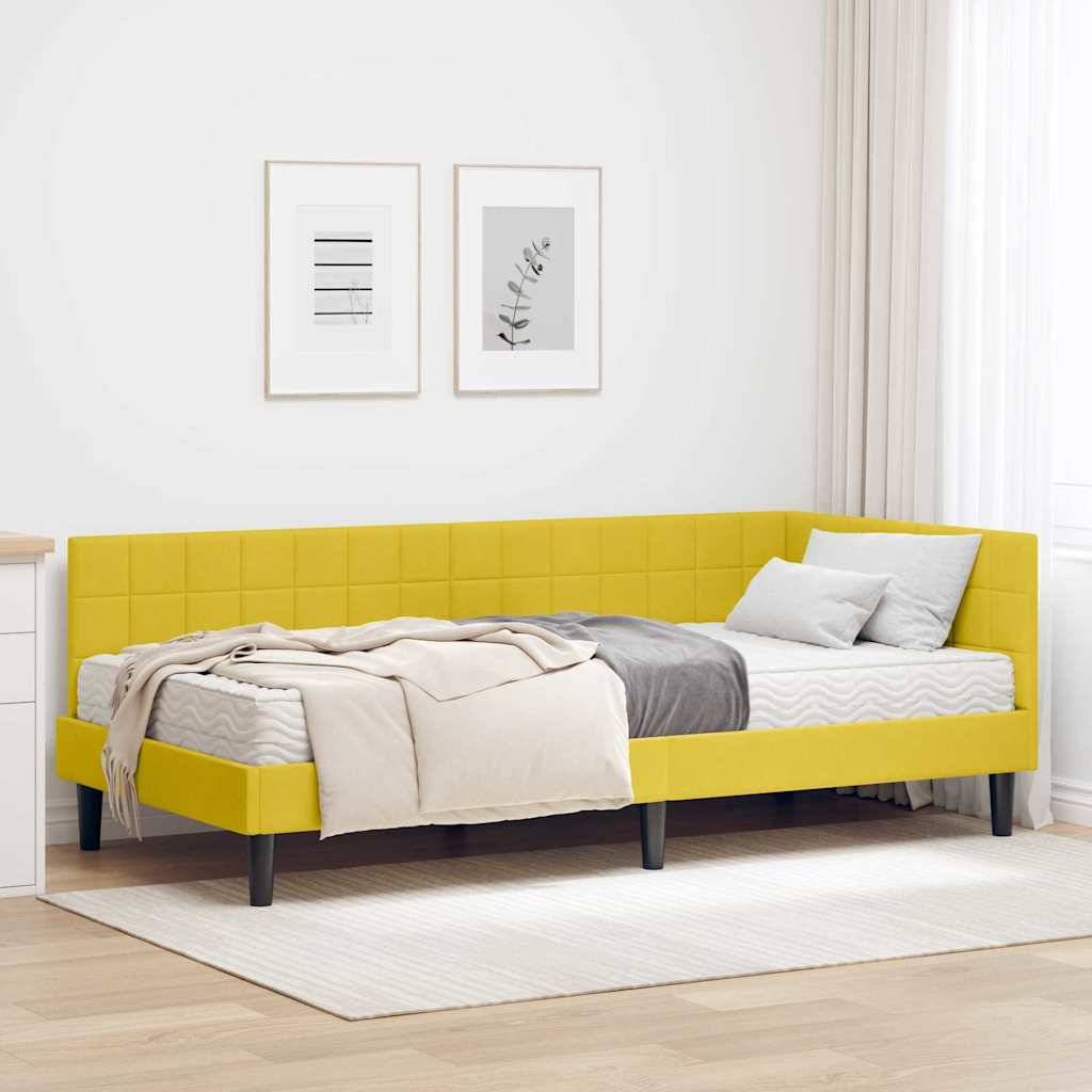 Ein modernes Schlafzimmer zeigt ein gelb gepolstertes Bett mit weißer und grauer Bettwäsche, vor einer weißen Wand mit gerahmten Kunstwerken.