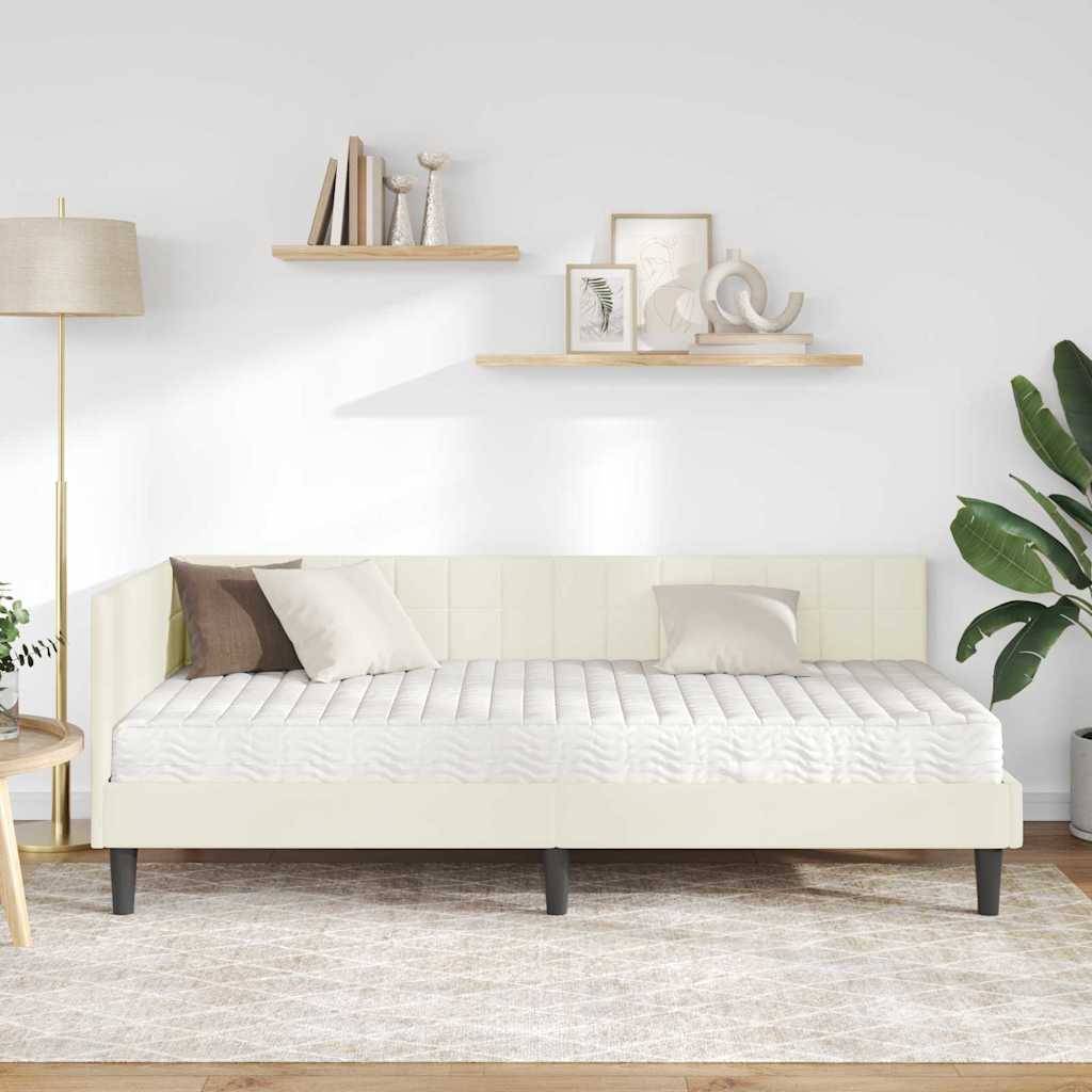 Ein minimalistisches Wohnzimmer mit einem weißen Tagesbett, einer beigen Lampe, Holzregalen mit Dekorationen und einer grünen Pflanze auf der rechten Seite.