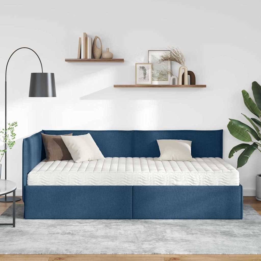Ein moderner Raum mit einer blauen Tagesbettkoje, bestückt mit beige und braunen Kissen, zwei an der Wand befestigten Regalen mit Deko und einer Topfpflanze neben einer geschwungenen Stehlampe.