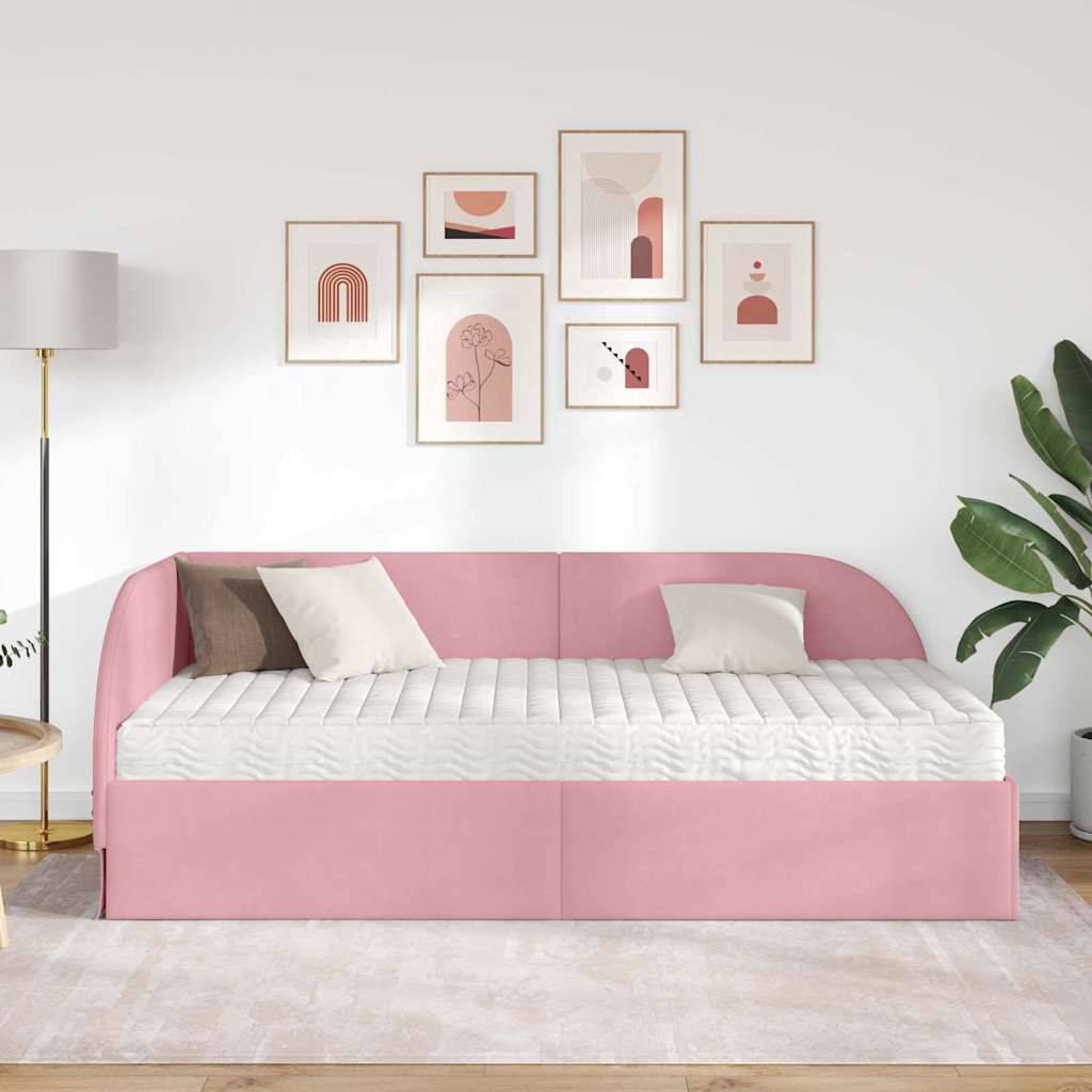 Ein modernes Wohnzimmer mit einem rosa Schlafsofa, zwei weißen Kissen, einer Galeriewand mit abstrakten Kunstwerken, einer großen Zimmerpflanze und einer Stehlampe.