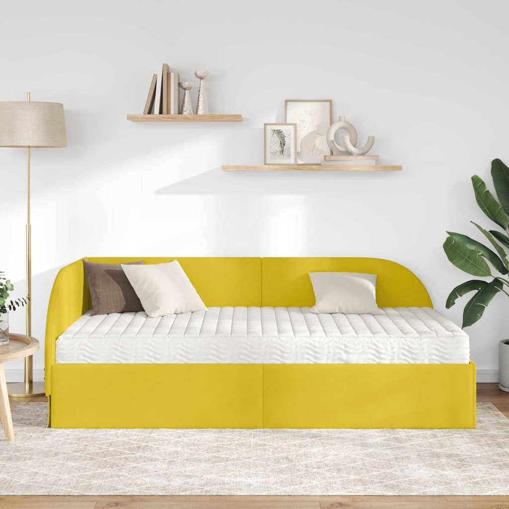Eine hellgelbe Schlafcouch mit einer gesteppten weißen Matratze und zwei Kissen in einem modernen Wohnzimmer mit Holzregalen und einer Stehlampe.