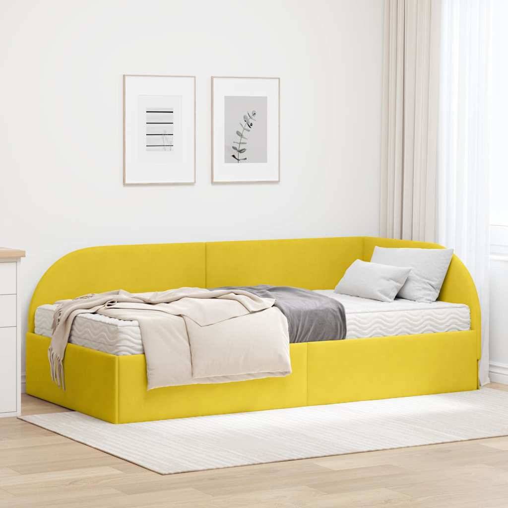 Gelbes Schlafsofa mit Kissen und Decken, vor einer weißen Wand mit gerahmter Kunst. Ein heller Teppich und Vorhang schaffen eine gemütliche Raumatmosphäre.
