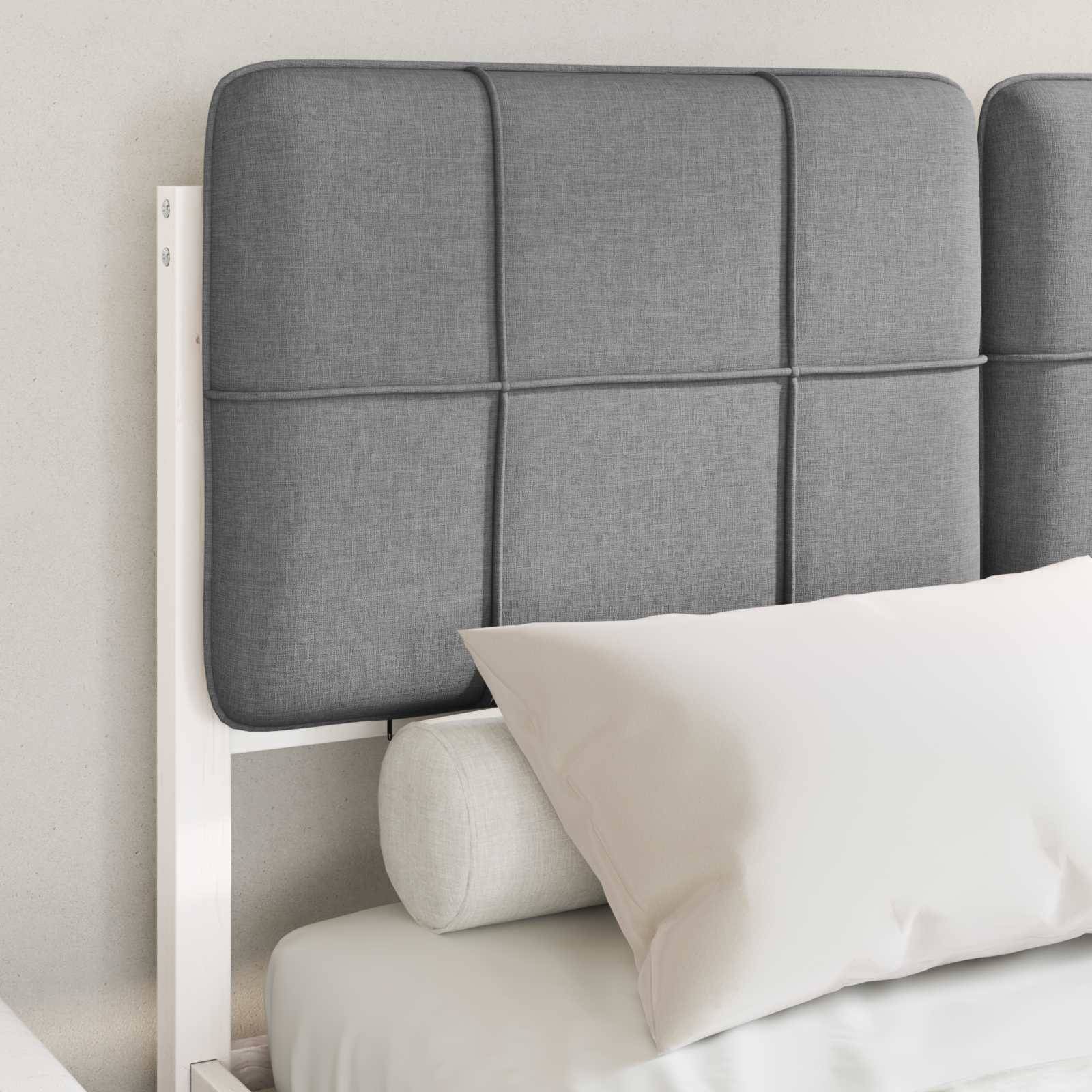 Ein ordentlich gemachtes Bett mit grau gepolstertem Kopfteil, weißen Kissen und einem zylindrischen Nackenrolle vor einer weißen Wand.