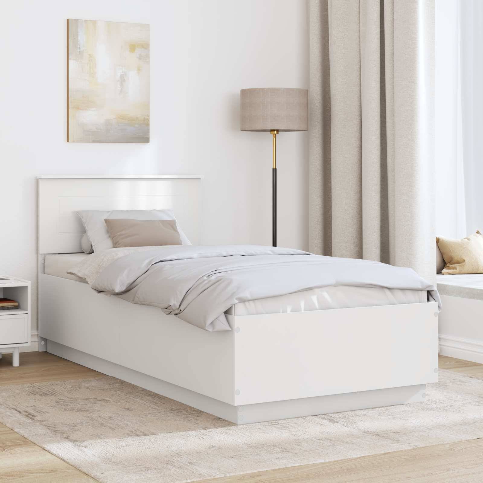 Ein aufgeräumtes Schlafzimmer zeigt ein sauber gemachtes weißes Bett mit grau-taupe Bettwäsche, eine Stehlampe und einen kleinen Nachttisch mit einem Buch und Dekoration.