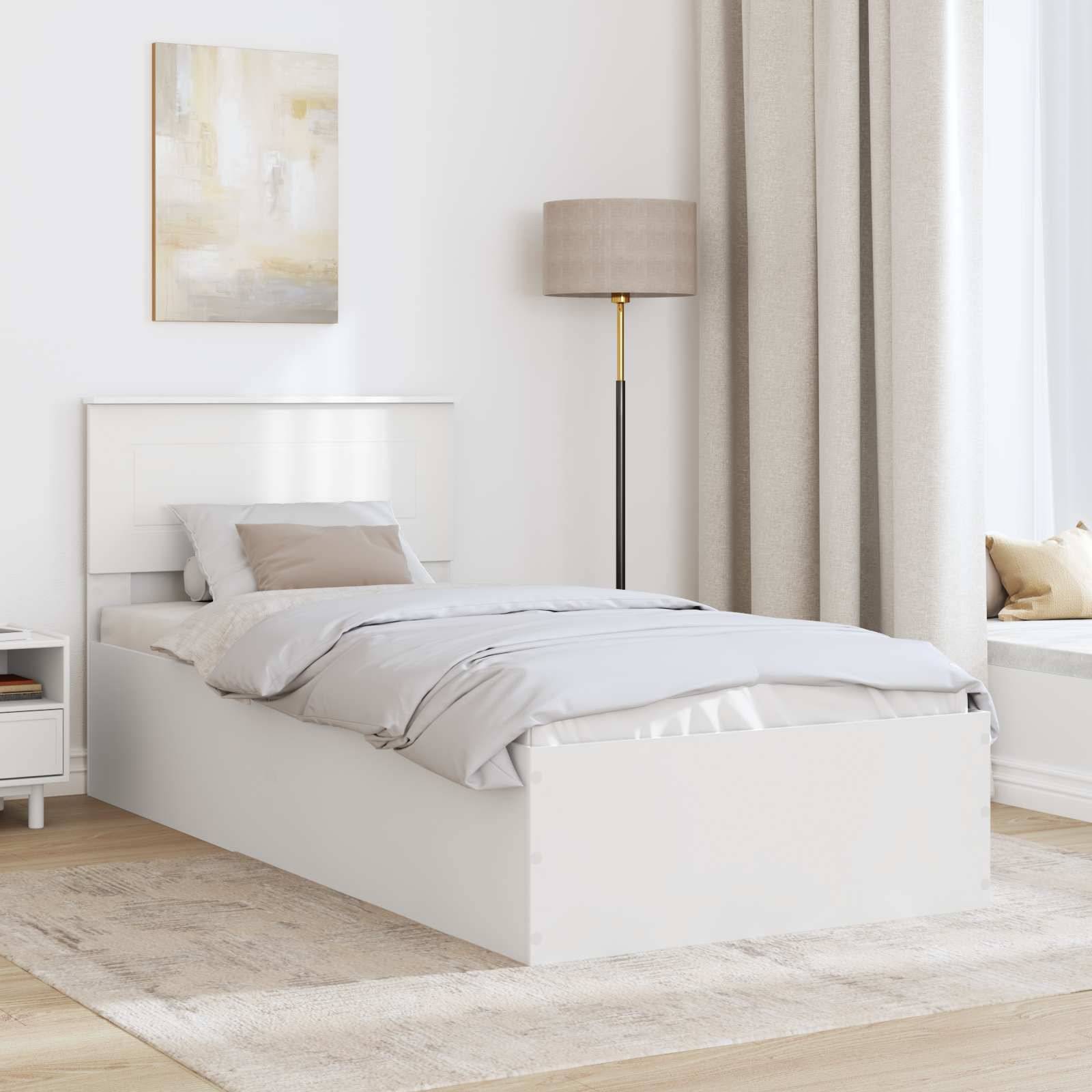 Ein minimalistisches Schlafzimmer mit einem weißen Bett, Nachttisch und Lampe. Beige Vorhänge und ein Gemälde verleihen Wärme. Sonnenlicht filtert durch ein großes Fenster.