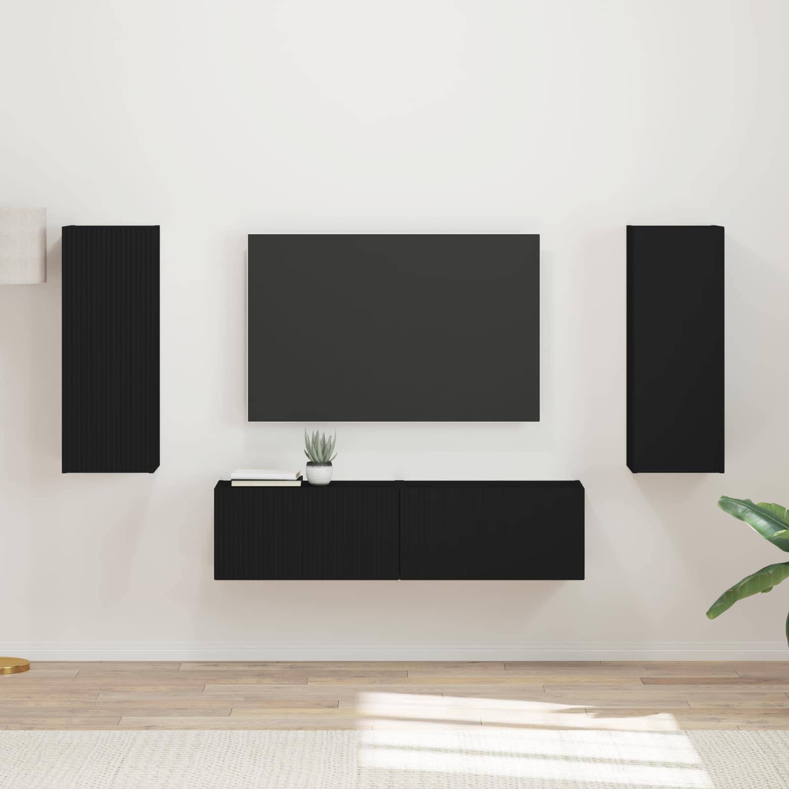 Ein minimalistisches Wohnzimmer-Setup mit einer an der Wand montierten TV, zwei hohen Lautsprechern zu beiden Seiten und einem niedrigen Schrank darunter, alles in Schwarz, an einer hellen Wand.