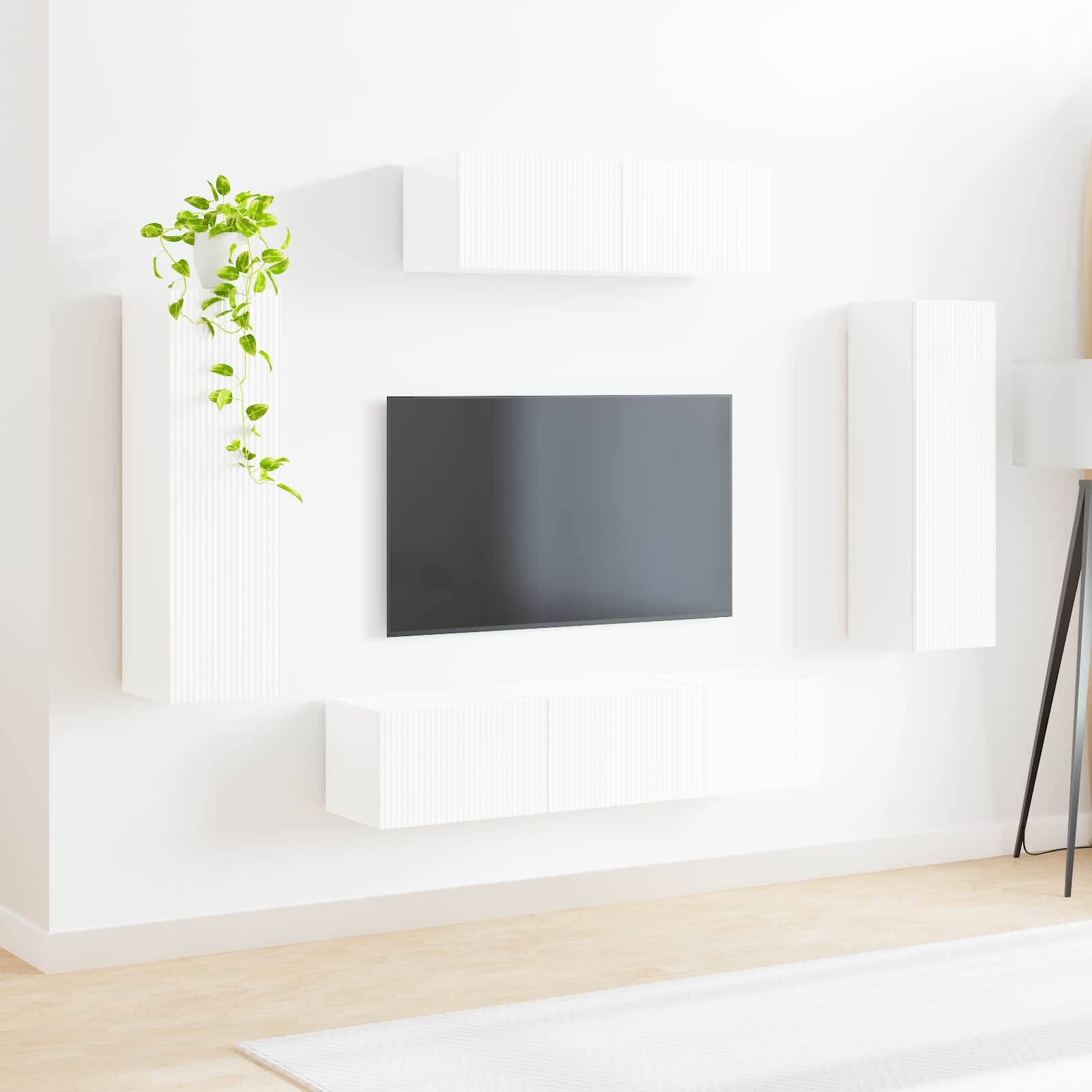 Ein minimalistisches Wohnzimmer mit einer wandmontierten TV, umgebenden weißen Schränken und einer kleinen grünen Pflanze, vor einer weißen Wand und einem Holzboden.