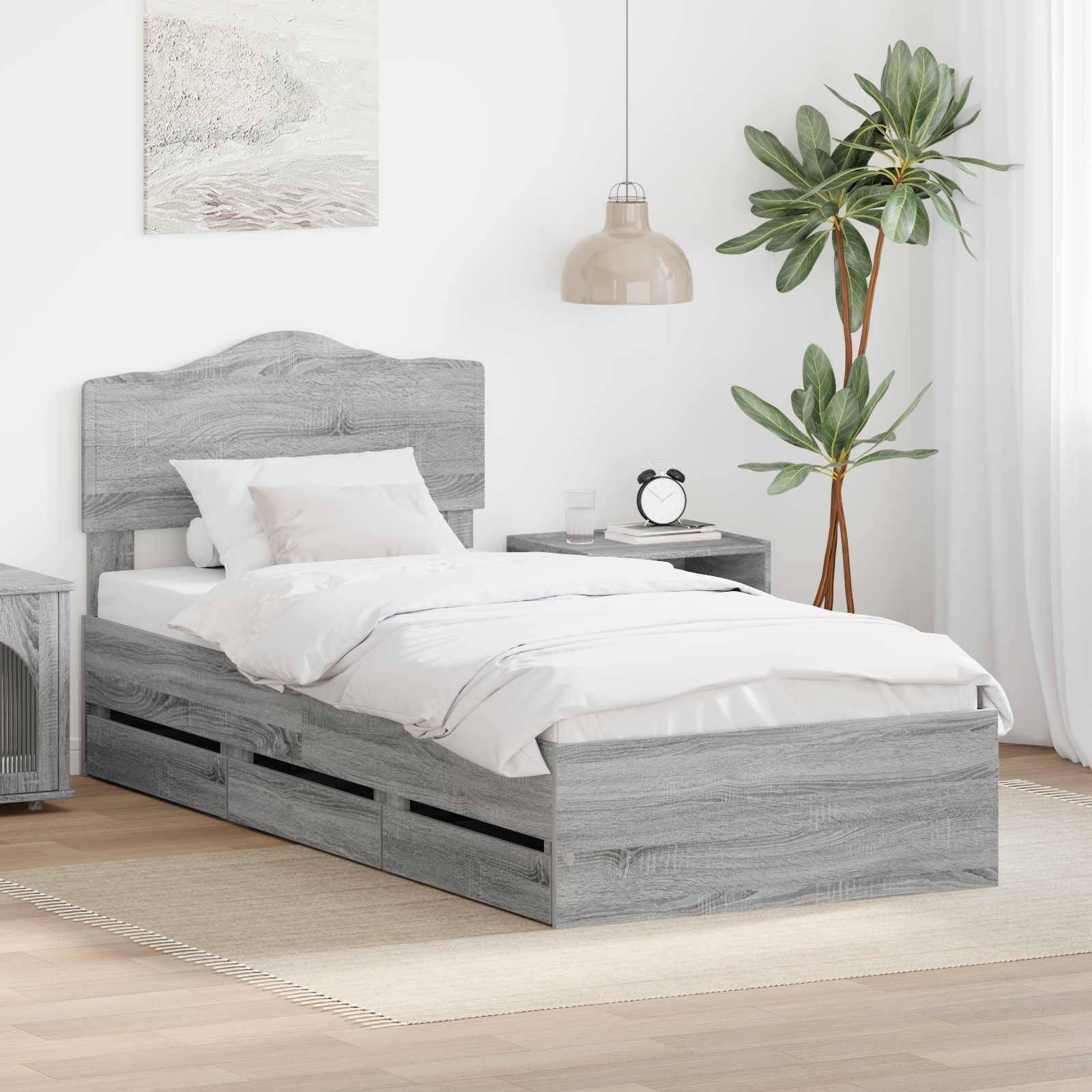 Ein gemütliches Schlafzimmer zeigt ein einzelnes graues Holzbett mit weißer Bettwäsche, einen Nachttisch mit einer Lampe, eine Topfpflanze und ein Wandkunstwerk.