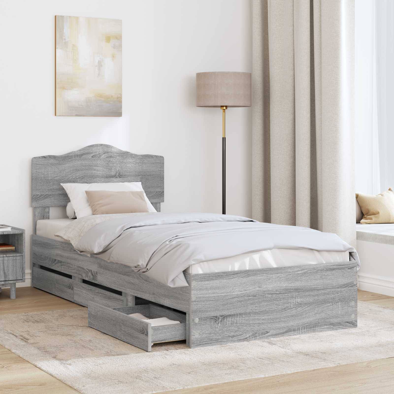 Ein ordentlich gemachtes Bett mit grauem Holzrahmen und Staurageschubladen darunter, neben einem Nachttisch und einer Lampe, in einem hellen Schlafzimmer.
