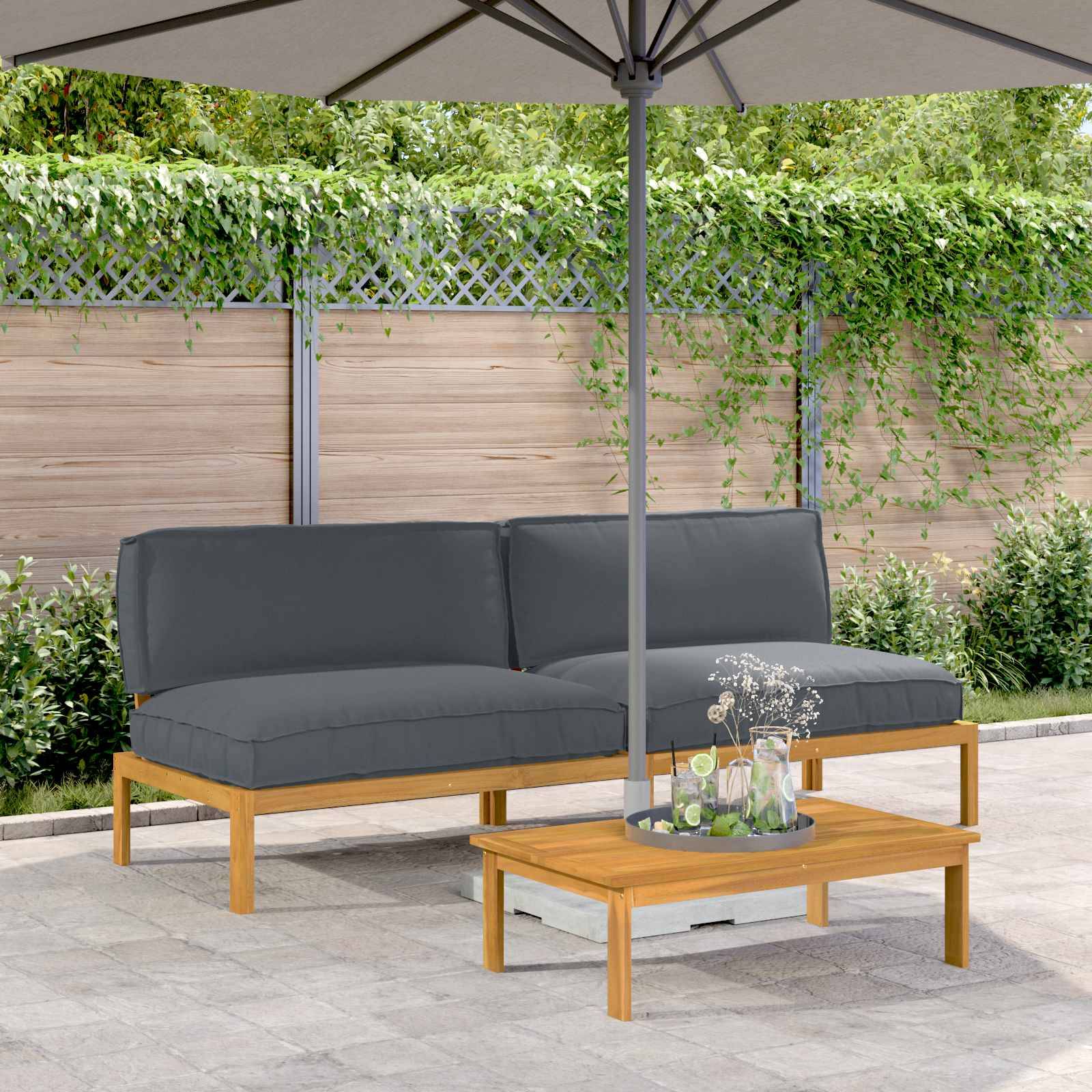 Außenterrasse mit einem grauen gepolsterten Sofa unter einem großen Sonnenschirm. Ein kleiner Holztisch trägt ein dekoratives Element. Grünpflanzen und Holzzaun im Hintergrund.