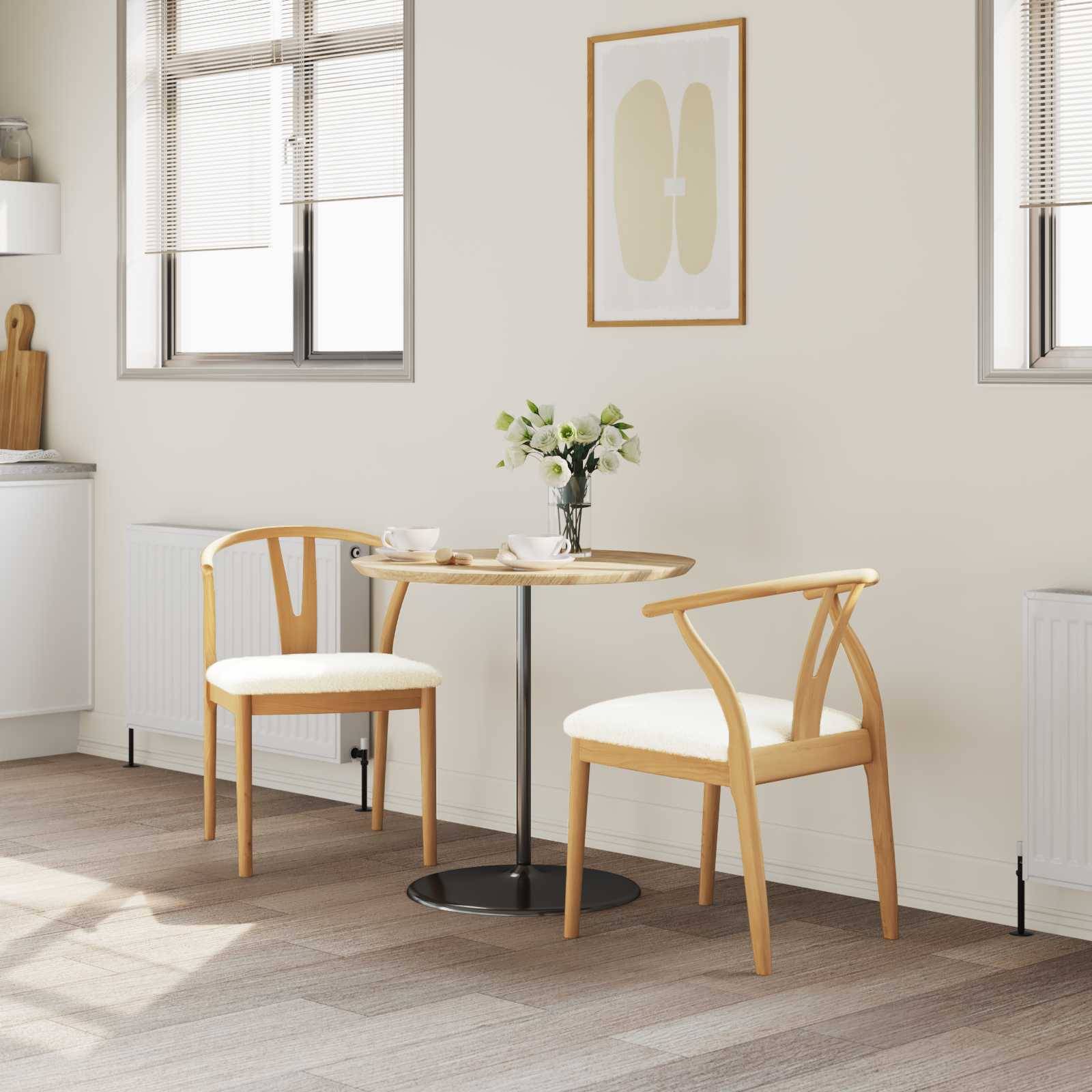 Ein kleiner Essbereich mit einem runden Tisch, zwei Holzstühlen mit weißen Kissen, einer Vase mit weißen Blumen und minimalistischer Wandkunst.