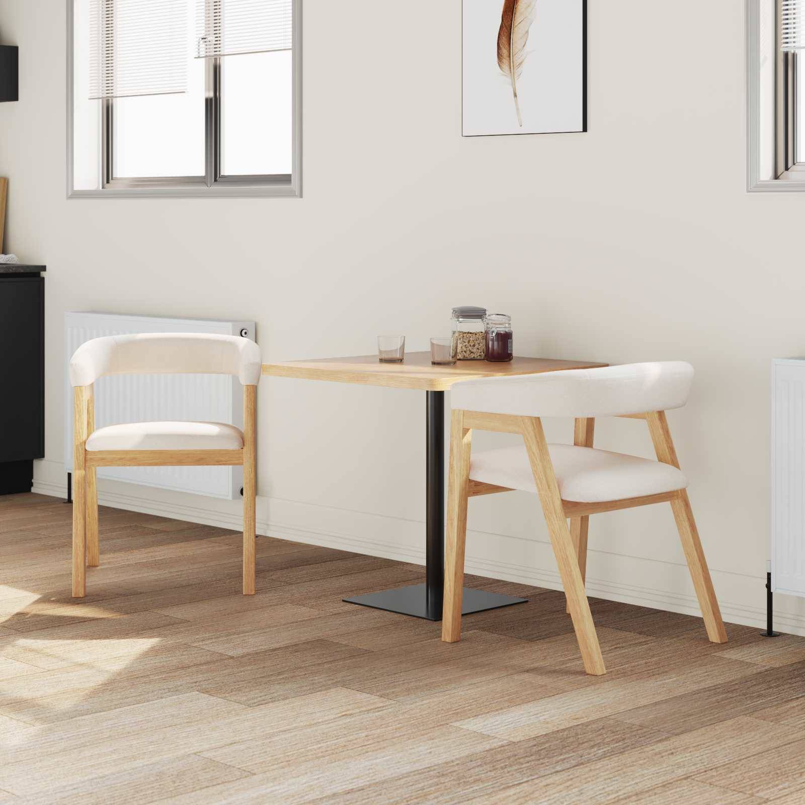 Eine minimalistische Küche mit einem kleinen Holz-Esstisch, zwei passenden Stühlen mit weißen Kissen und neutraler Dekoration. Warmes natürliches Licht.