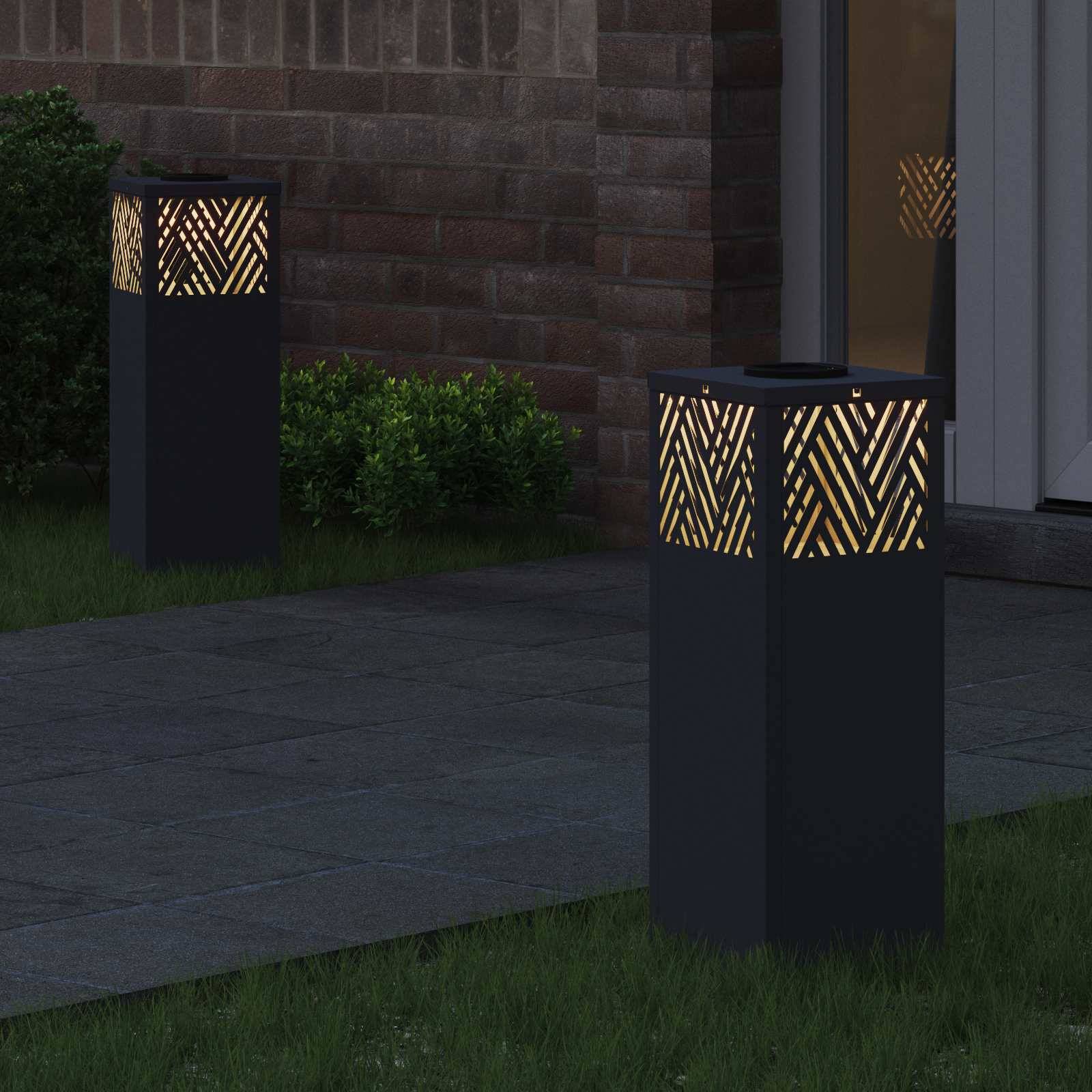 Außenlampen auf einer Terrasse mit geometrischem Muster strahlen warmes Licht in der Nähe einer Tür aus und verstärken die Abendatmosphäre mit sanfter Beleuchtung.