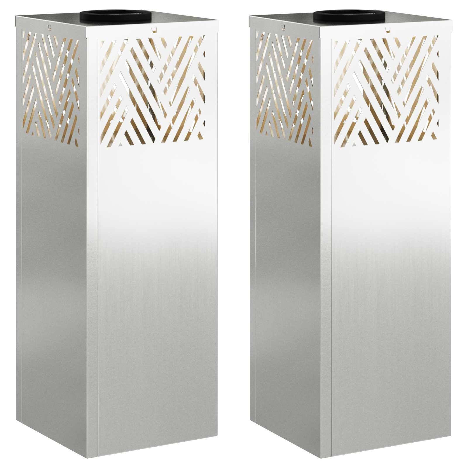 Zwei hohe silberne Metalllampenmasten mit geometrischen Ausschnittsdesigns im oberen Bereich, die nebeneinander vor einem einfarbigen Hintergrund stehen.