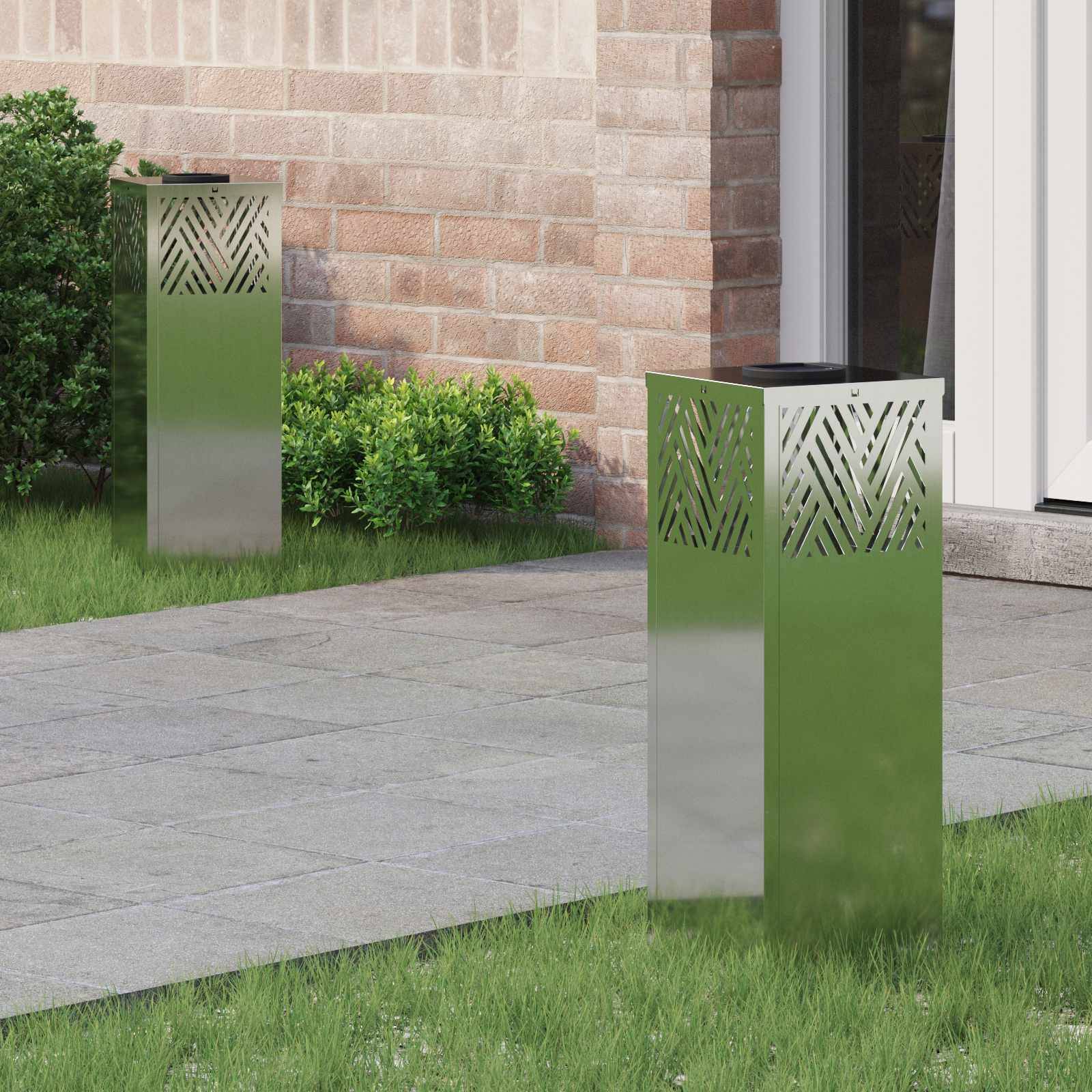 Zwei moderne metallische Gartenleuchten auf einem Steinweg neben einem Backsteingebäude, umgeben von einem gepflegten Rasen und kleinen Sträuchern.