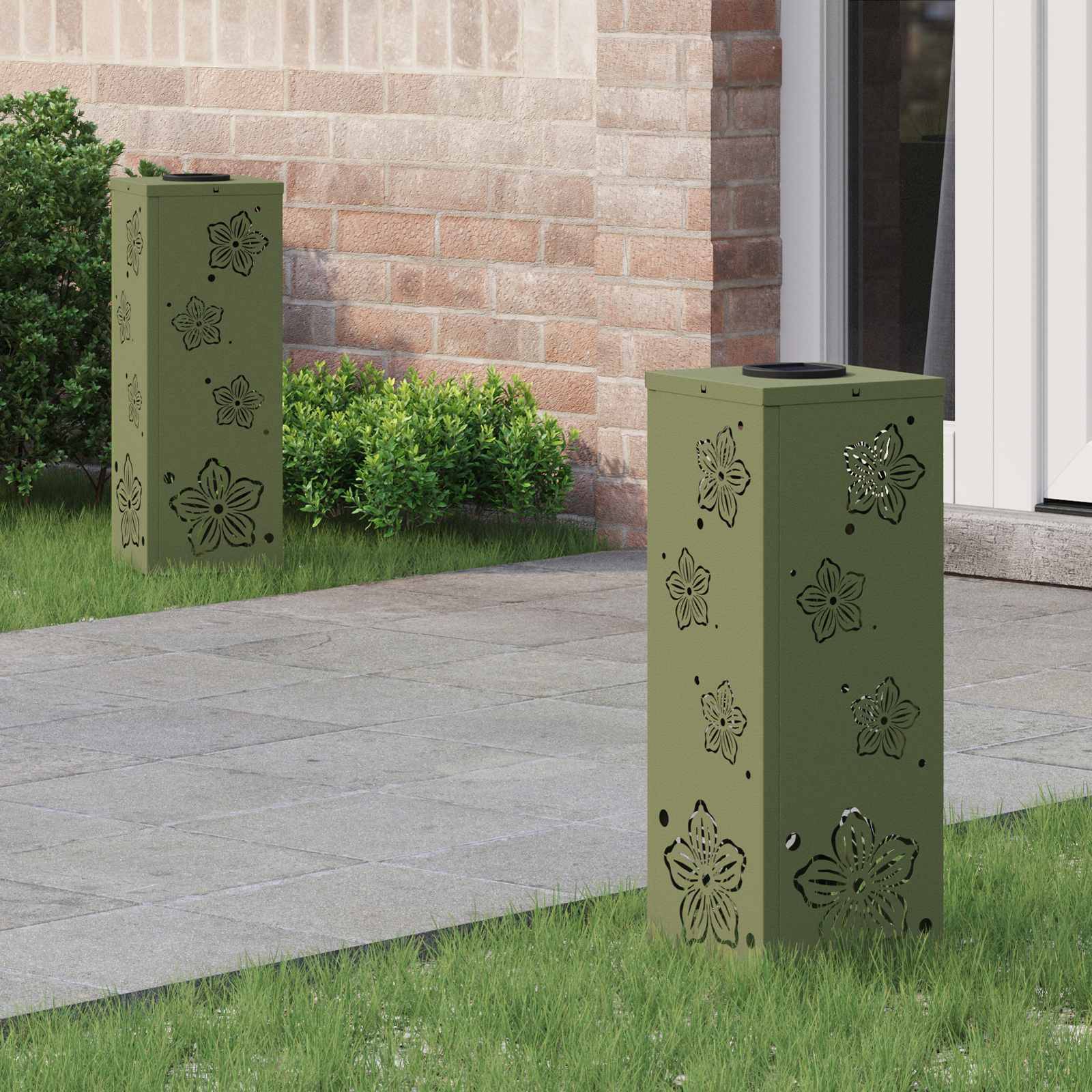 Zwei dekorative grüne Säulen mit floralen Ausschnitten stehen auf einer Terrasse neben einem Gebäudeeingang. Büsche und Gras säumen den Gehweg.