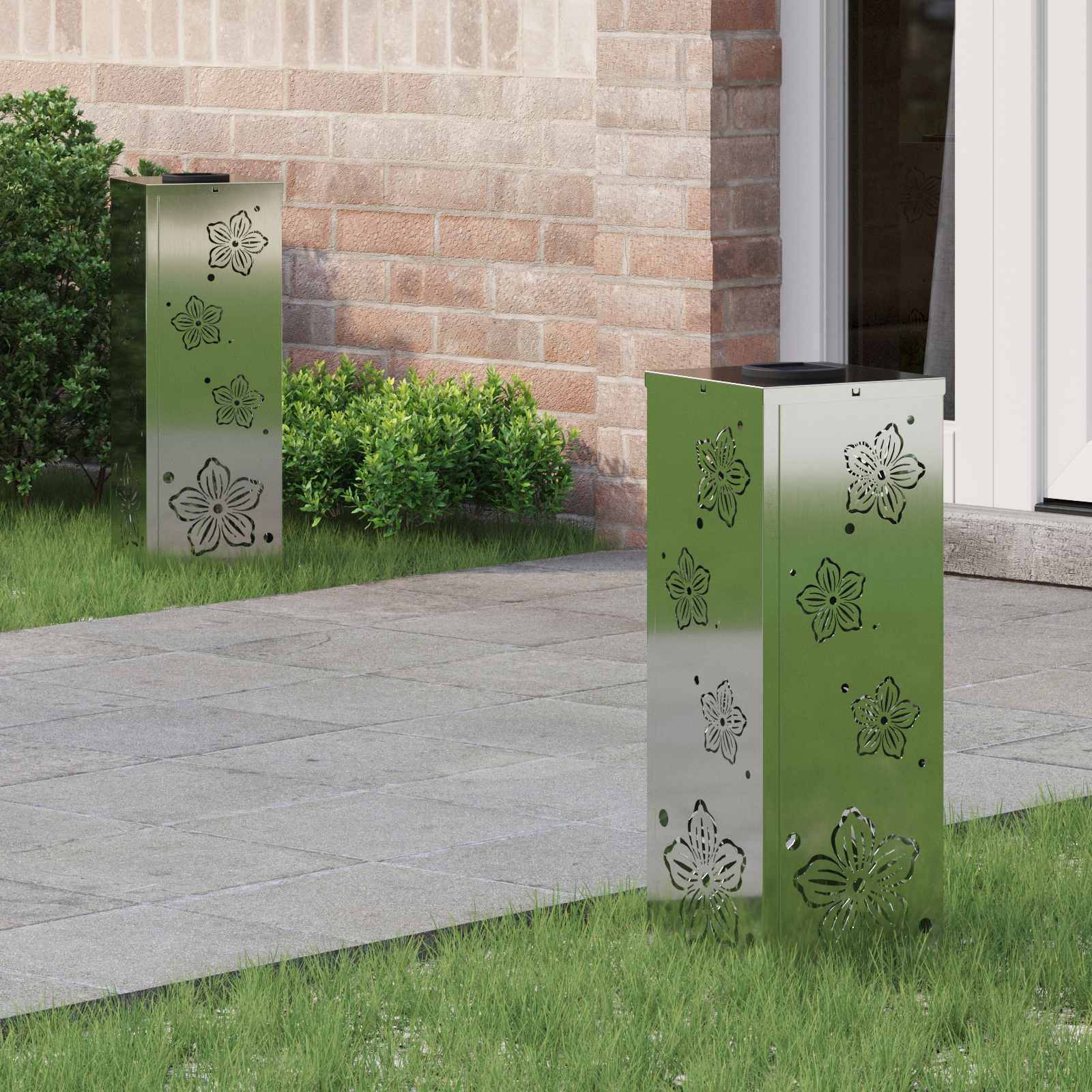 Zwei metallische Säulen mit Blumenreliefs stehen auf einer Rasenfläche in der Nähe eines Ziegelgebäudeeingangs, teilweise von Grünpflanzen gerahmt.