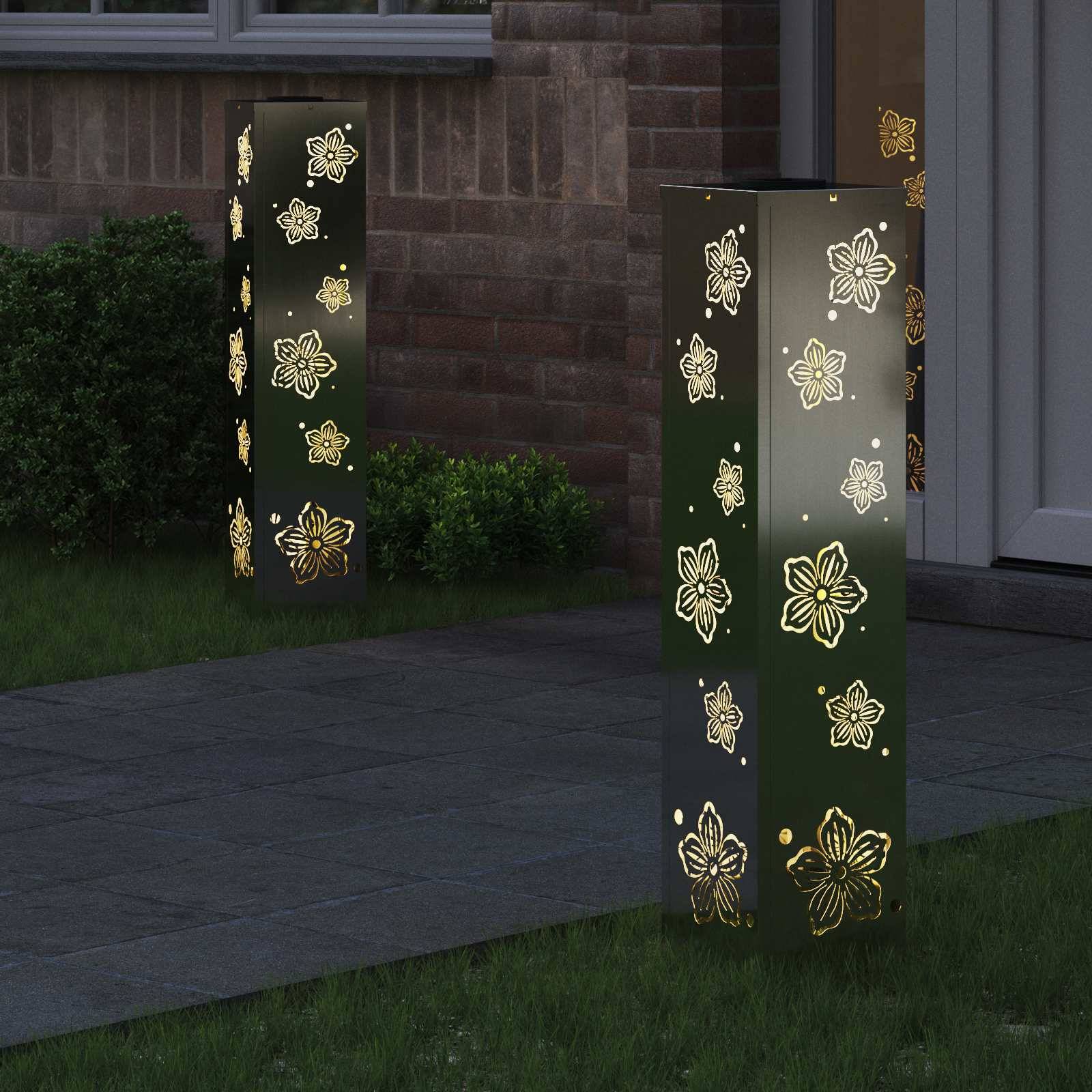 Garten im Freien mit dekorativen Laternen, die beleuchtete Blumenmuster aufweisen und ein warmes Leuchten auf das umgebende Gras und die Ziegelwand werfen.