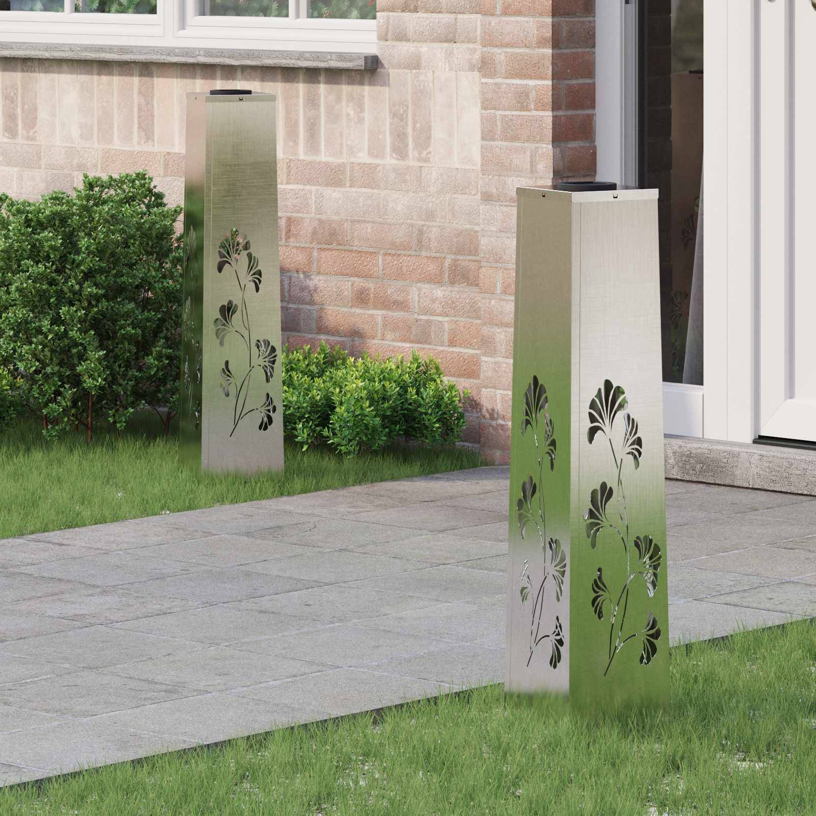 Zwei Metallgartenleuchten mit Blattmustern stehen auf einem gepflasterten Weg in der Nähe eines Hauseingangs, umgeben von grünem Rasen und Büschen.