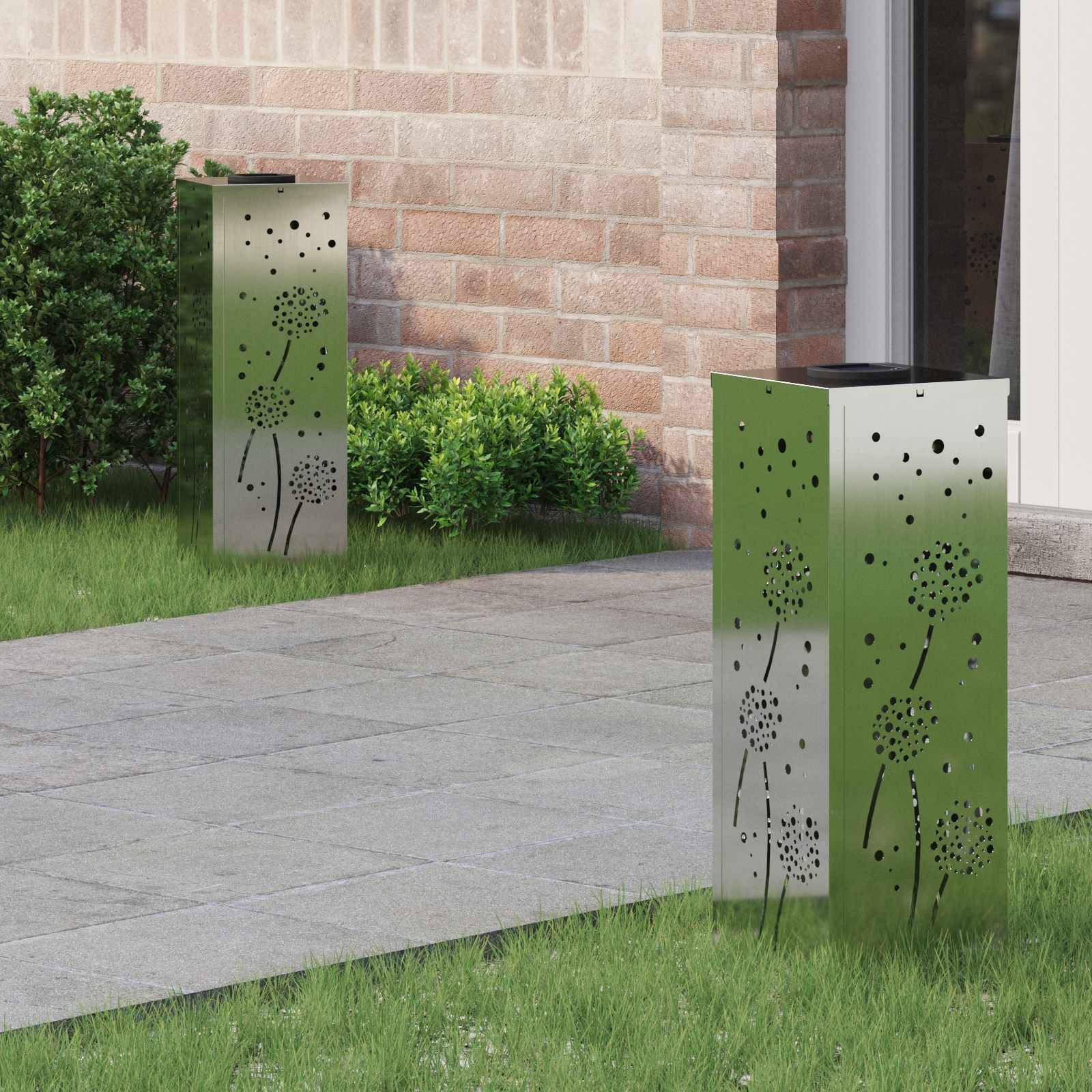 Zwei hohe Metallgartenlaternen mit Löwenzahnmustern auf einem Steinweg in der Nähe von Grünpflanzen und einem Ziegelgebäude.