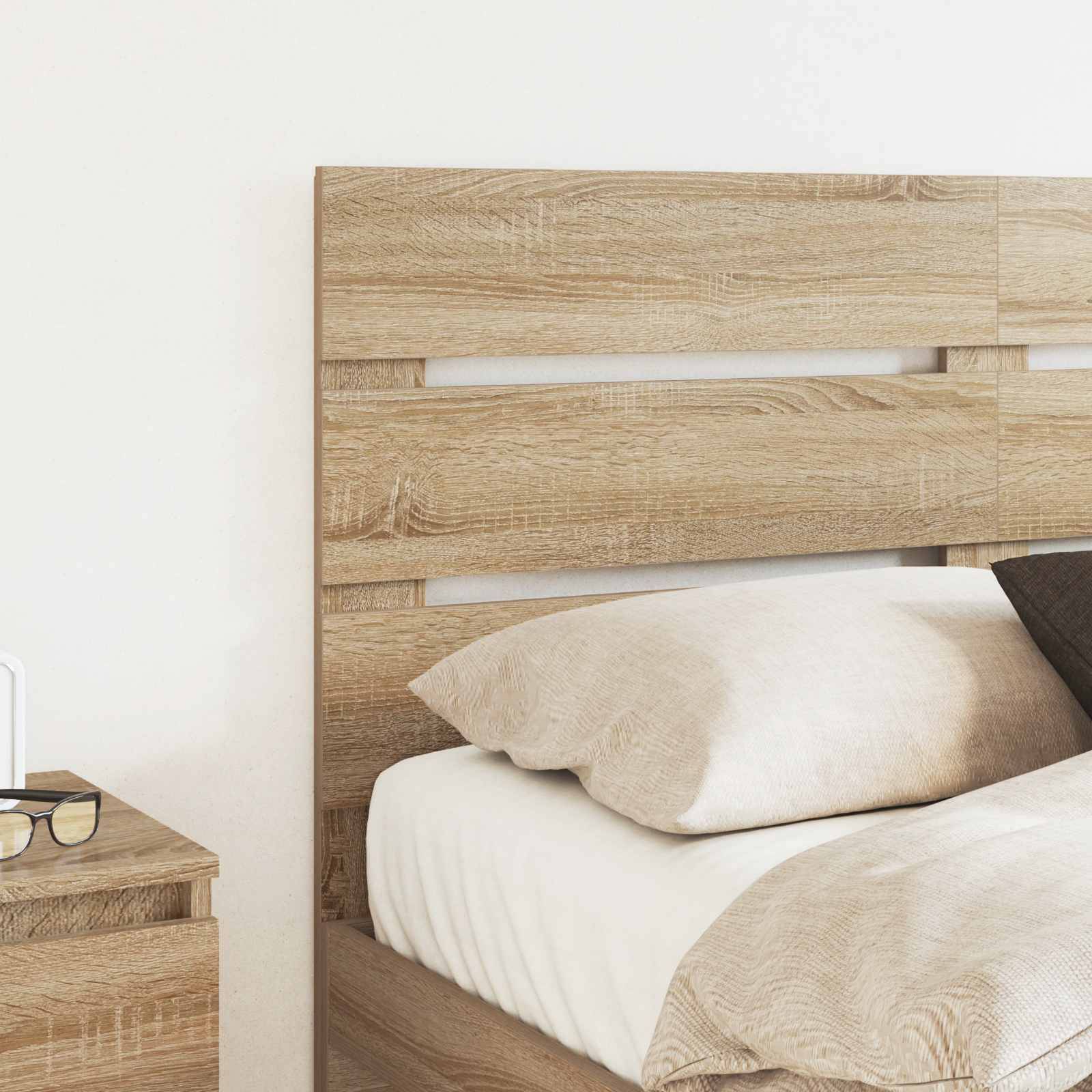 Ein ordentlich gemachtes Bett mit beigen Betttüchern und Holzkopfteil steht neben einem kleinen Tisch mit einem Buch in einem warm beleuchteten Zimmer.