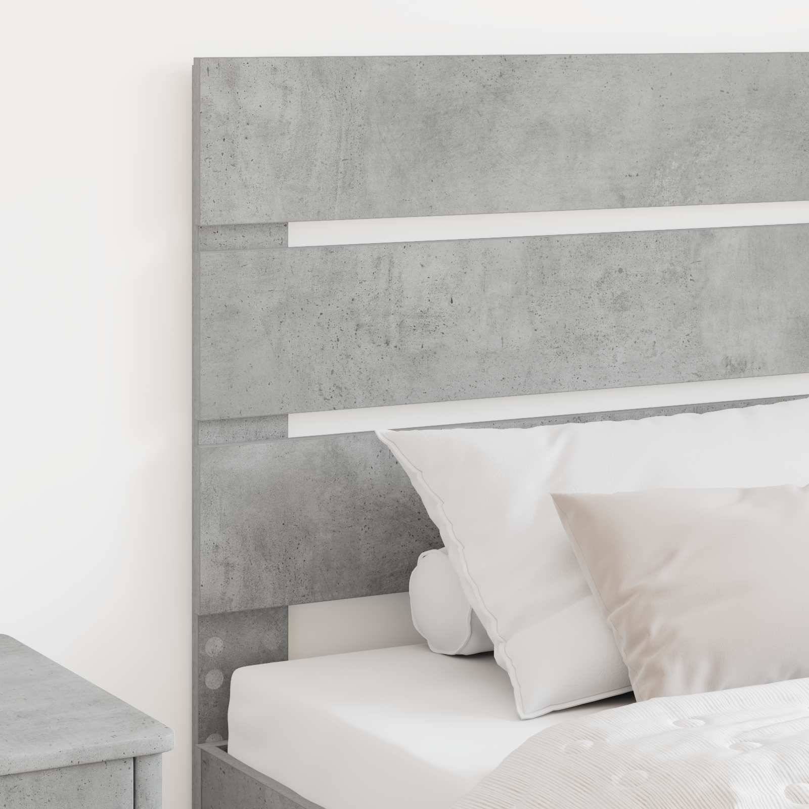 Ein modernes Bett mit kopfende im Betonoptik und zwei weißen Kissen, eines aufrecht angeordnet und das andere leicht schräg, auf einer weißen Bettdecke.