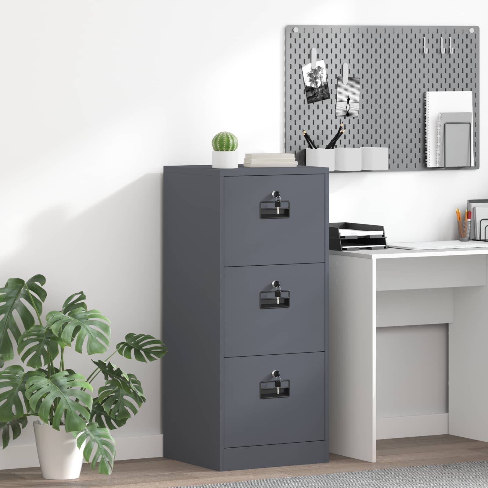 Ein grauer dreiteiliger Aktenschrank neben einem weißen Schreibtisch in einem Arbeitszimmer, mit einer Topfpflanze und einer Pinnwand an der Wand oben.