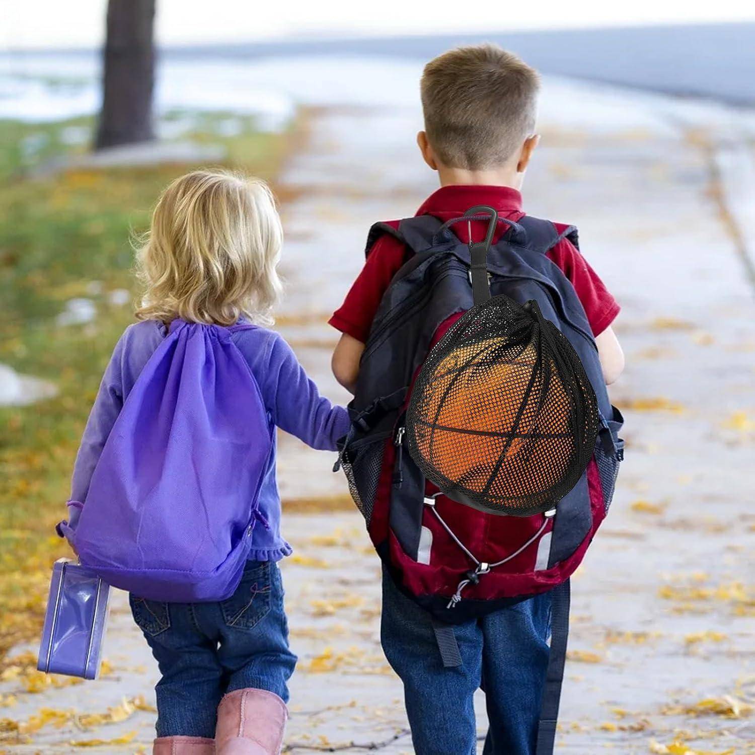 Ein junges Mädchen und ein Junge, beide mit Rucksäcken, gehen zusammen auf einem laubbedeckten Weg und halten sich an den Händen. Der Junge trägt einen Basketball.