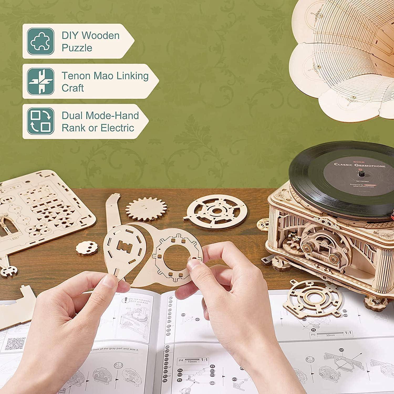 Hände, die ein hölzernes mechanisches Puzzle zusammenbauen, neben einem teilweise zusammengebauten Grammophon-Modell auf einem Tisch mit einer Schritt-für-Schritt-Anleitung.