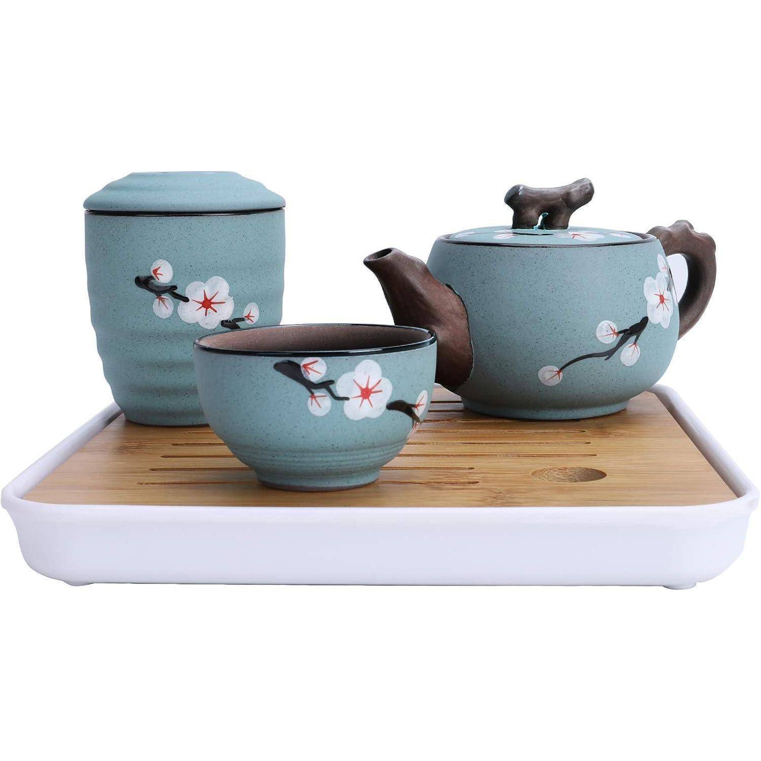 Ein Teeservice aus Keramik mit Kirschblütendesign umfasst eine Teekanne, eine Tasse und einen Behälter auf einem Bambus-Tablett.