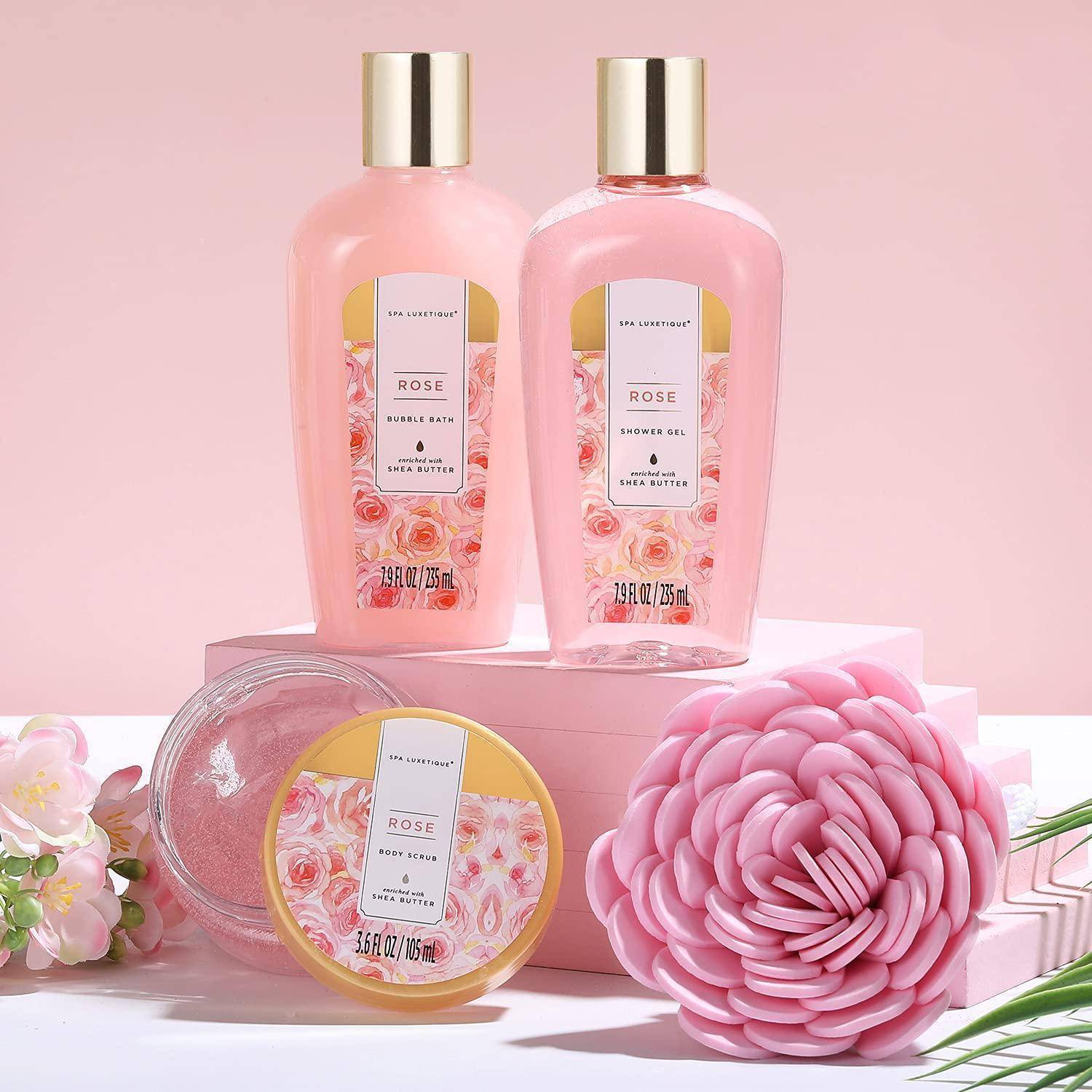 Rosenduftende Badeprodukte wie Duschgel, Schaumbad, Körpercreme und dekorative Seife, auf einer rosa Oberfläche mit Blumen angeordnet.