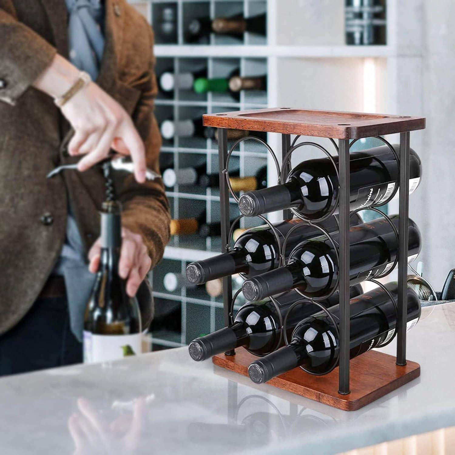 Eine Person in einer braunen Jacke öffnet eine Weinflasche neben einem Weinregal aus Holz, das neun Flaschen enthält, mit einem größeren Weinregal im Hintergrund.