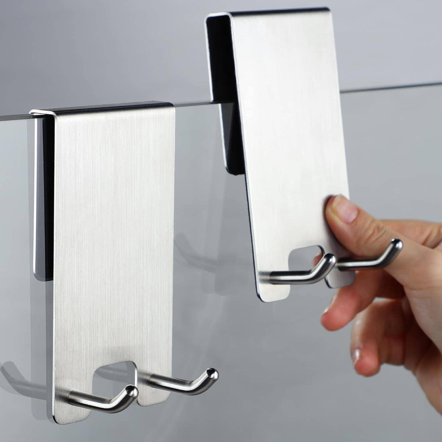 Eine Hand platziert einen metallischen Doppelhaken über eine Glasoberfläche und demonstriert die einfache Installation eines Tür- oder Schrankaufhängehakens.