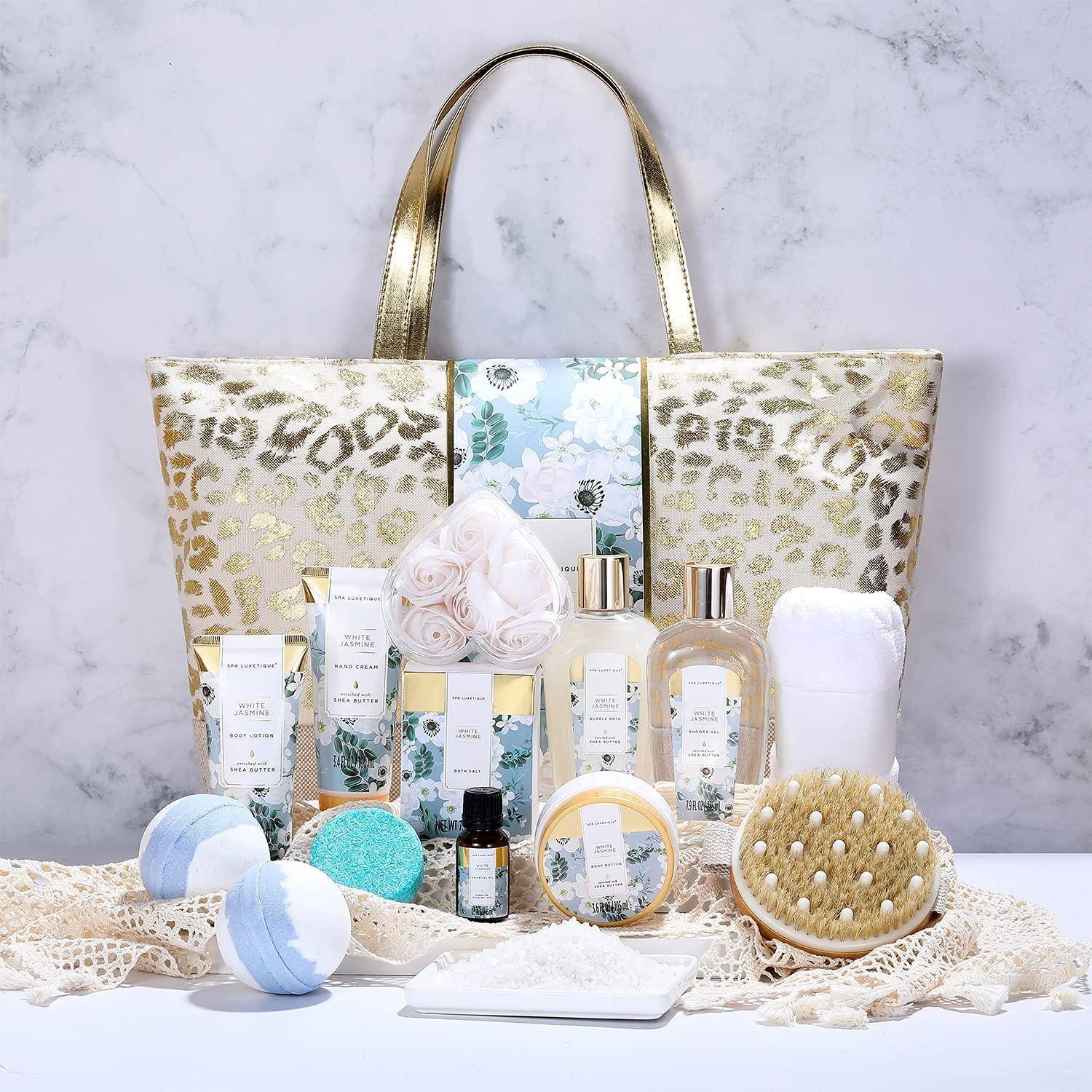 Eine gold- und blumenmustrige Tragetasche mit Spa-Produkten, darunter Lotionen, Badebomben, ätherische Öle und eine Bürste mit natürlichen Borsten auf einem Spitzenuntersetzer.