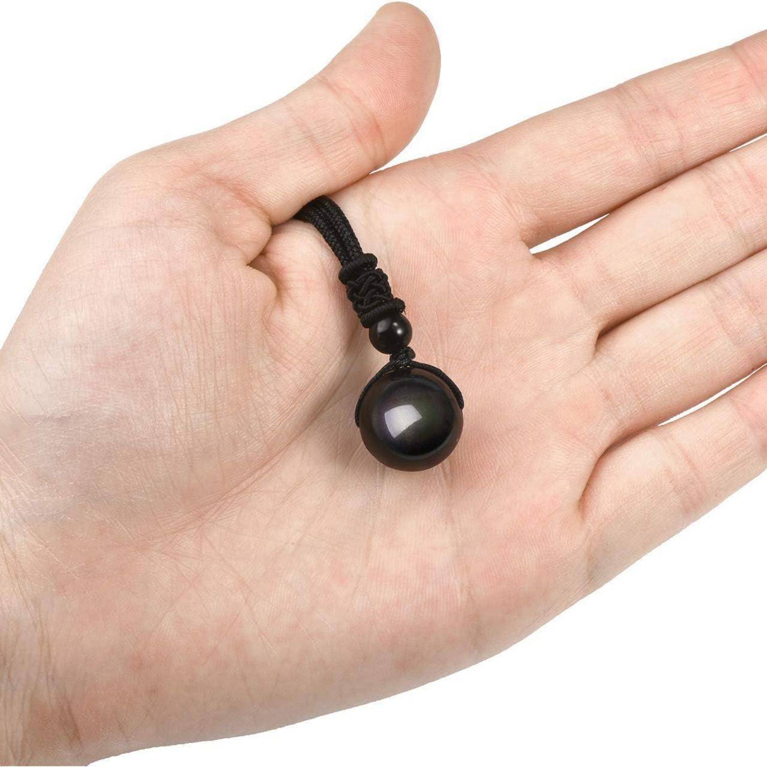 Eine Hand hält eine kleine, glänzend schwarze Perle, die an einem geflochtenen schwarzen Seil befestigt ist und deren glatte Oberfläche und reflektierende Qualität zur Geltung bringt.