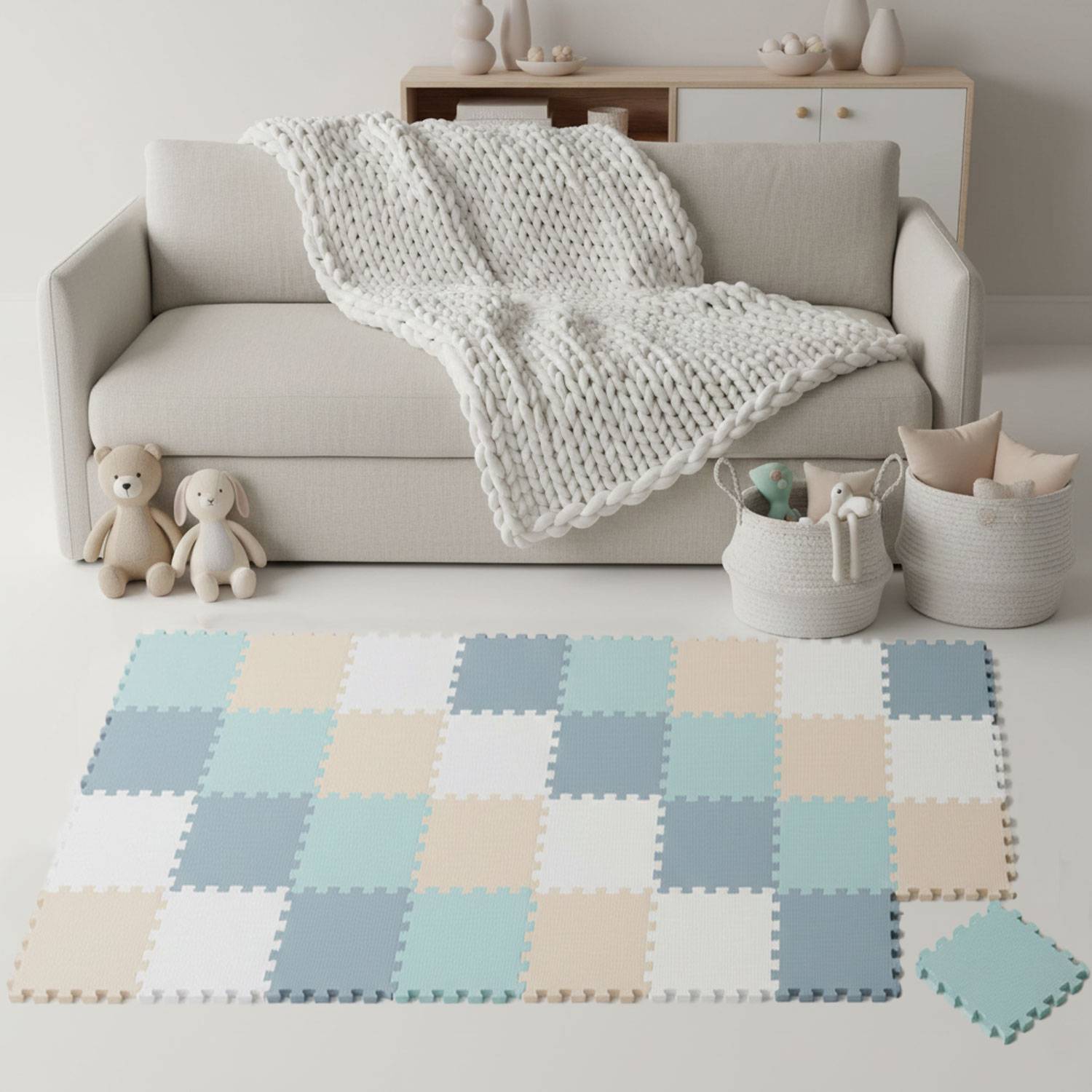 Ein gemütliches Wohnzimmer mit einem beigen Sofa, das mit einer gestrickten Decke behangen ist. Zwei Plüschtiere sitzen auf dem Boden neben einem geflochtenen Korb.