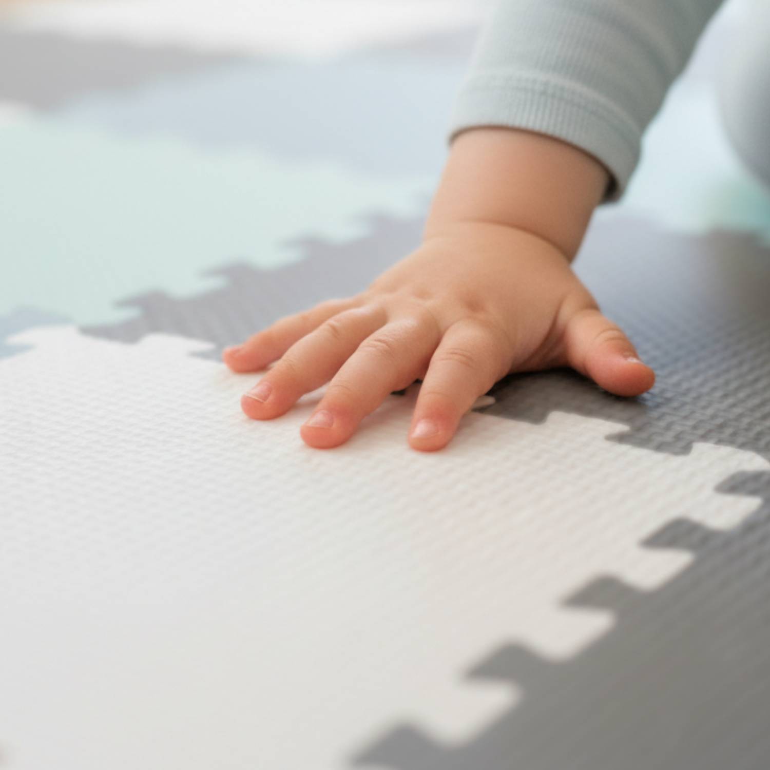 Eine Babyhand ruht auf einer weichen grauen und weißen Schaumstoff-Spielmatte und deutet auf eine sichere und fürsorgliche Spielumgebung hin.