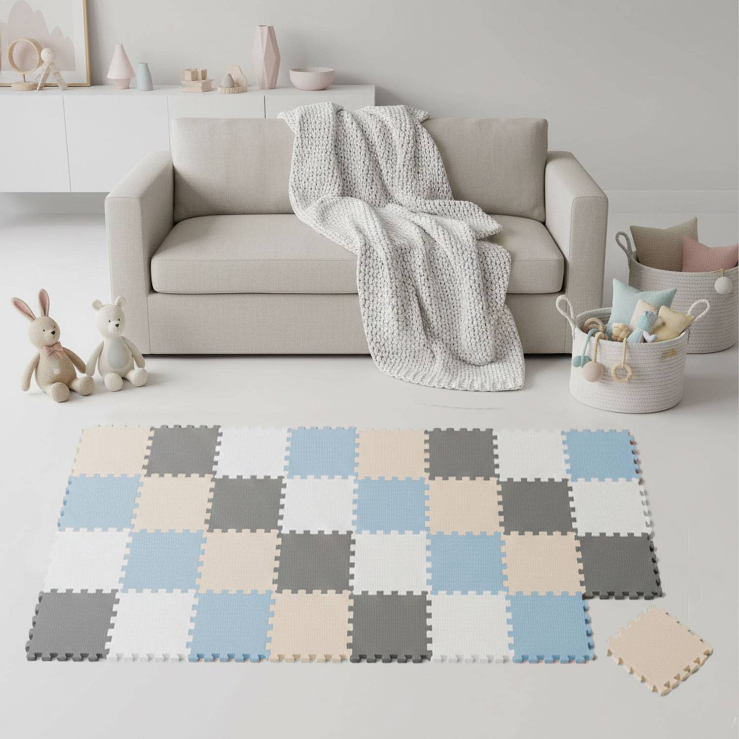 Ein gemütliches Wohnzimmer mit einem beigen Sofa, das mit einer gestrickten Decke überzogen ist, umgeben von kuscheligen Plüschtieren und pastellfarbenen Schaumstoffplatten auf dem Boden.