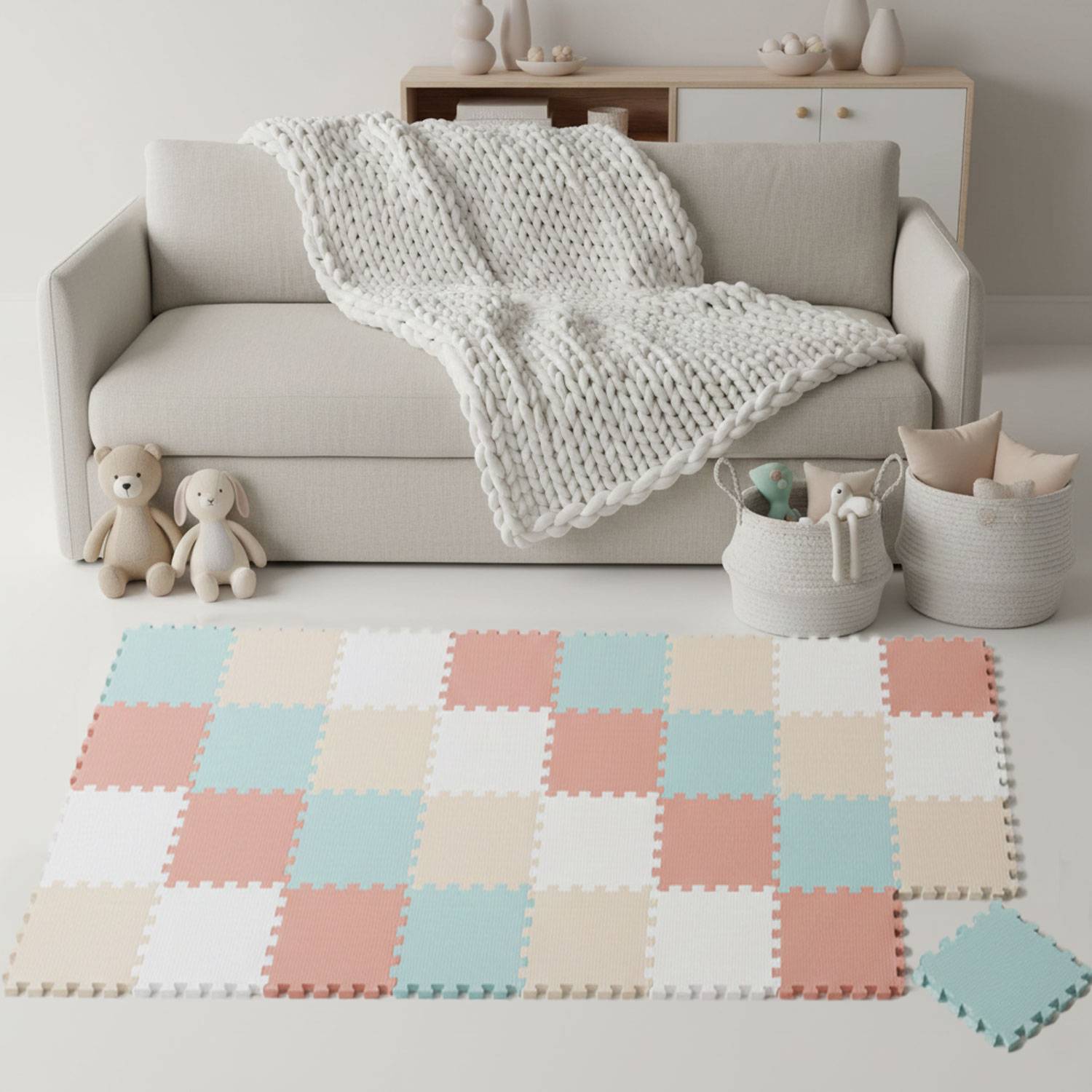 Ein gemütliches Wohnzimmer zeigt eine beige Couch mit einer gestrickten Decke, Spielzeugen und einer verschachtelten Schaumstoffmatte in Pastellfarben auf dem Boden.
