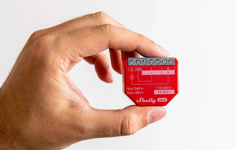 Eine Hand hält ein kleines rotes elektrisches Gerät mit der Aufschrift „Shelly Gen1