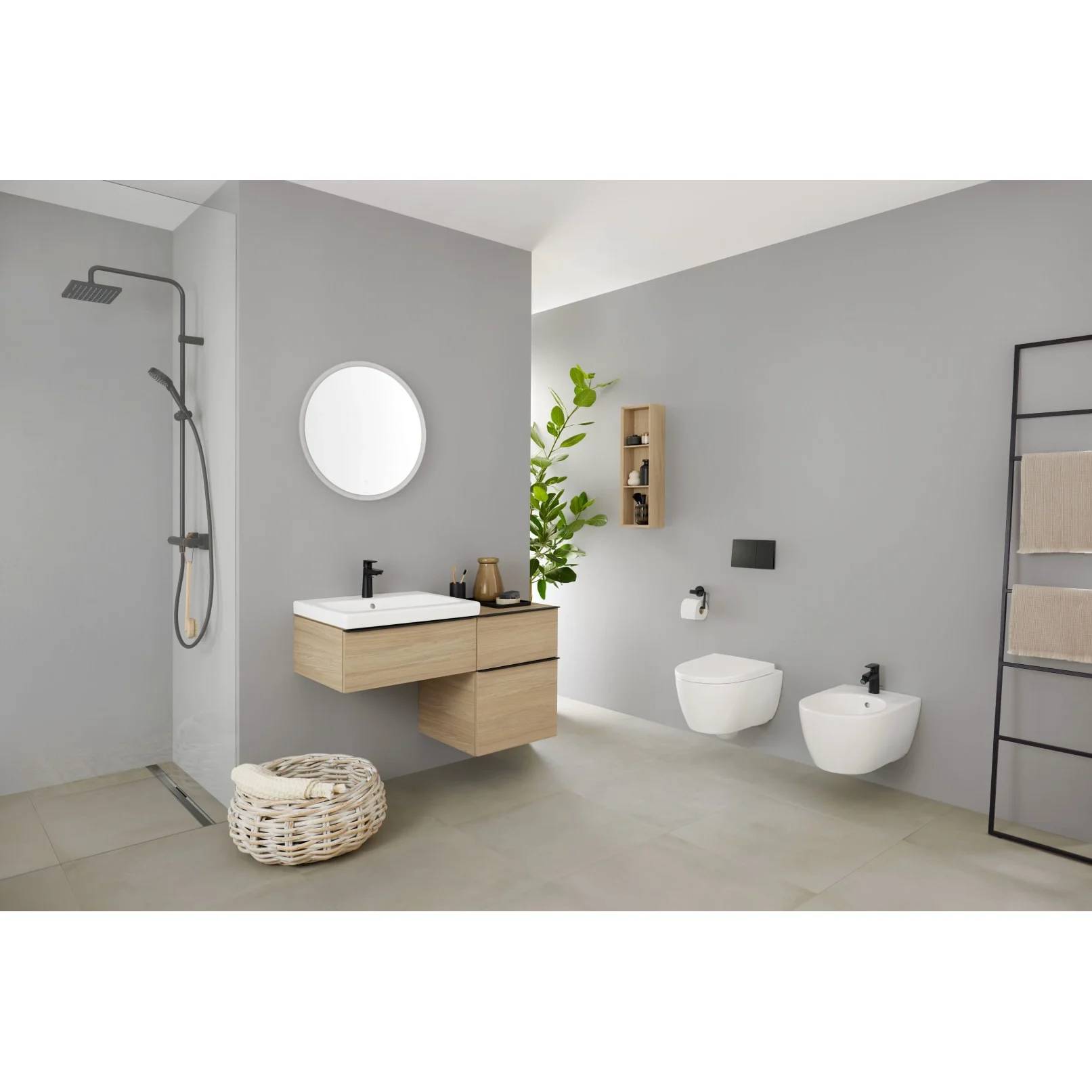 Modernes minimalistisches Badezimmer mit an der Wand montiertem Waschtisch, rundem Spiegel, Dusche, Toilette, Bidet, Handtuchleiter und gewebtem Korb auf hellem grauem Boden.