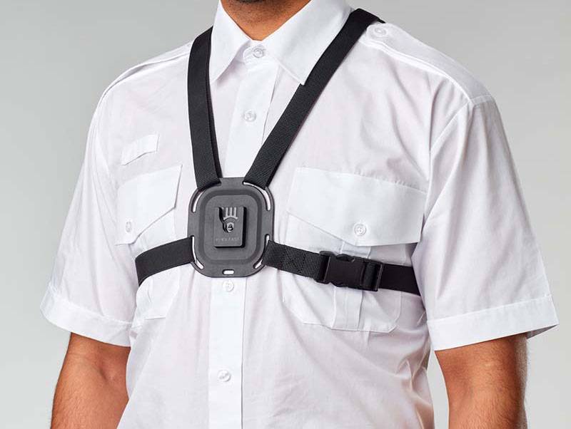Eine Person trägt ein weißes Hemd mit einer angebrachten Überwachungskamera auf der Brust, die mit schwarzen Riemen befestigt ist. Die Anordnung deutet auf die Verwendung von tragbarer Überwachung hin.