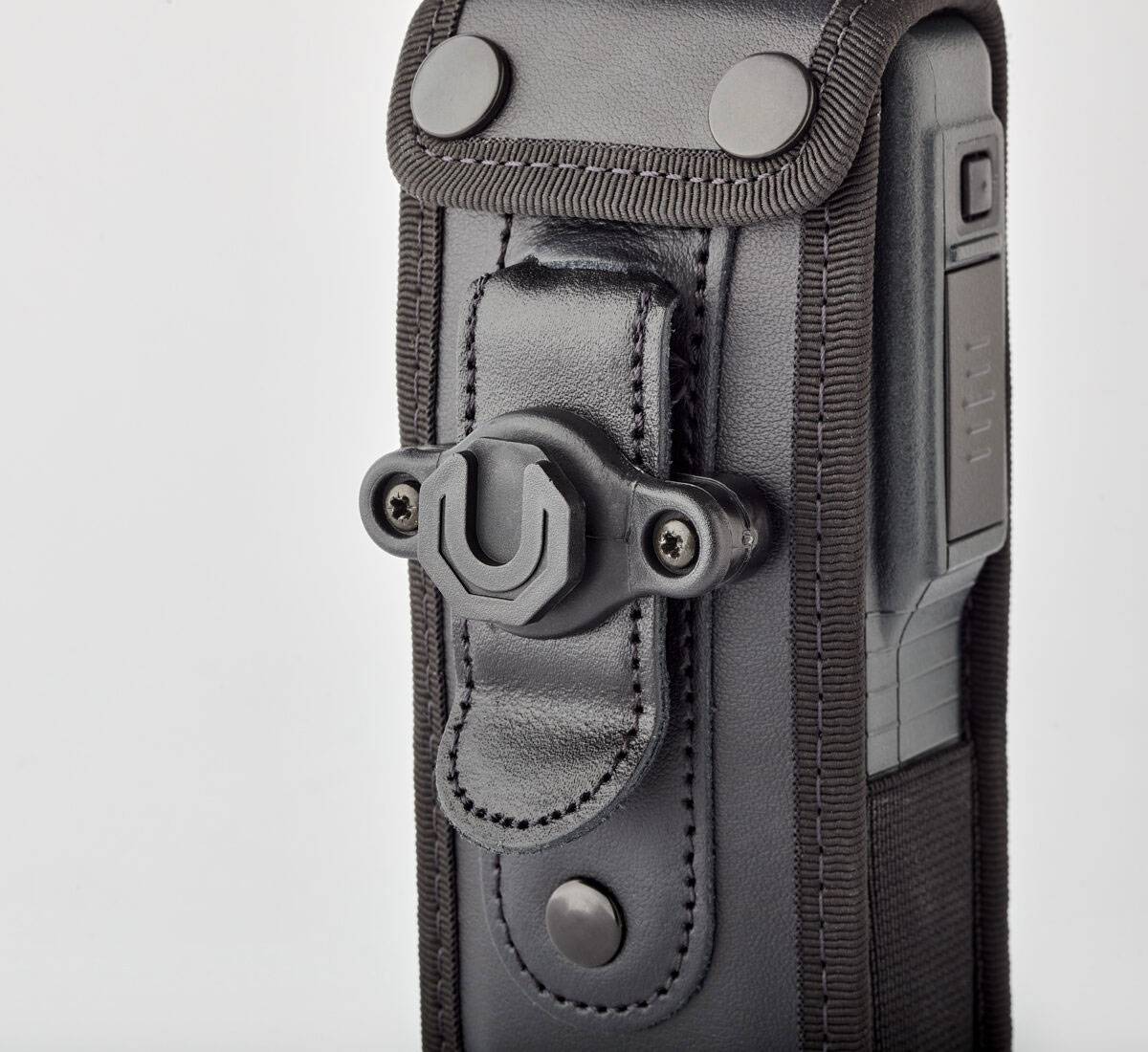 Eine Nahaufnahme eines schwarzen Lederkoffers mit Druckknopfverschluss, der ein teilweise sichtbares elektronisches Gerät enthält. Der Koffer hat eine Gürtelschlaufe.